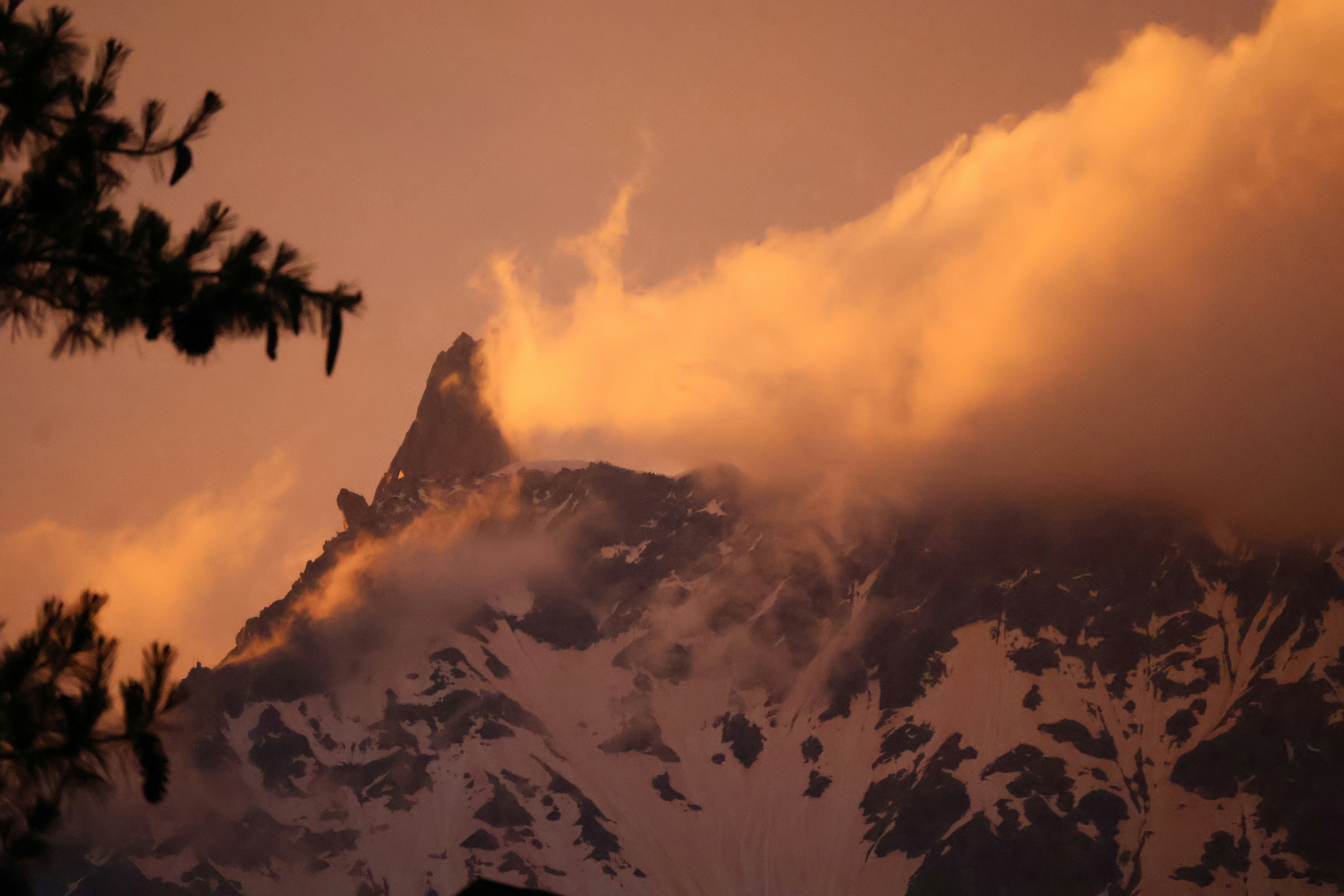 Snowy mountain peak partially obscured by clouds in warm golden hour light