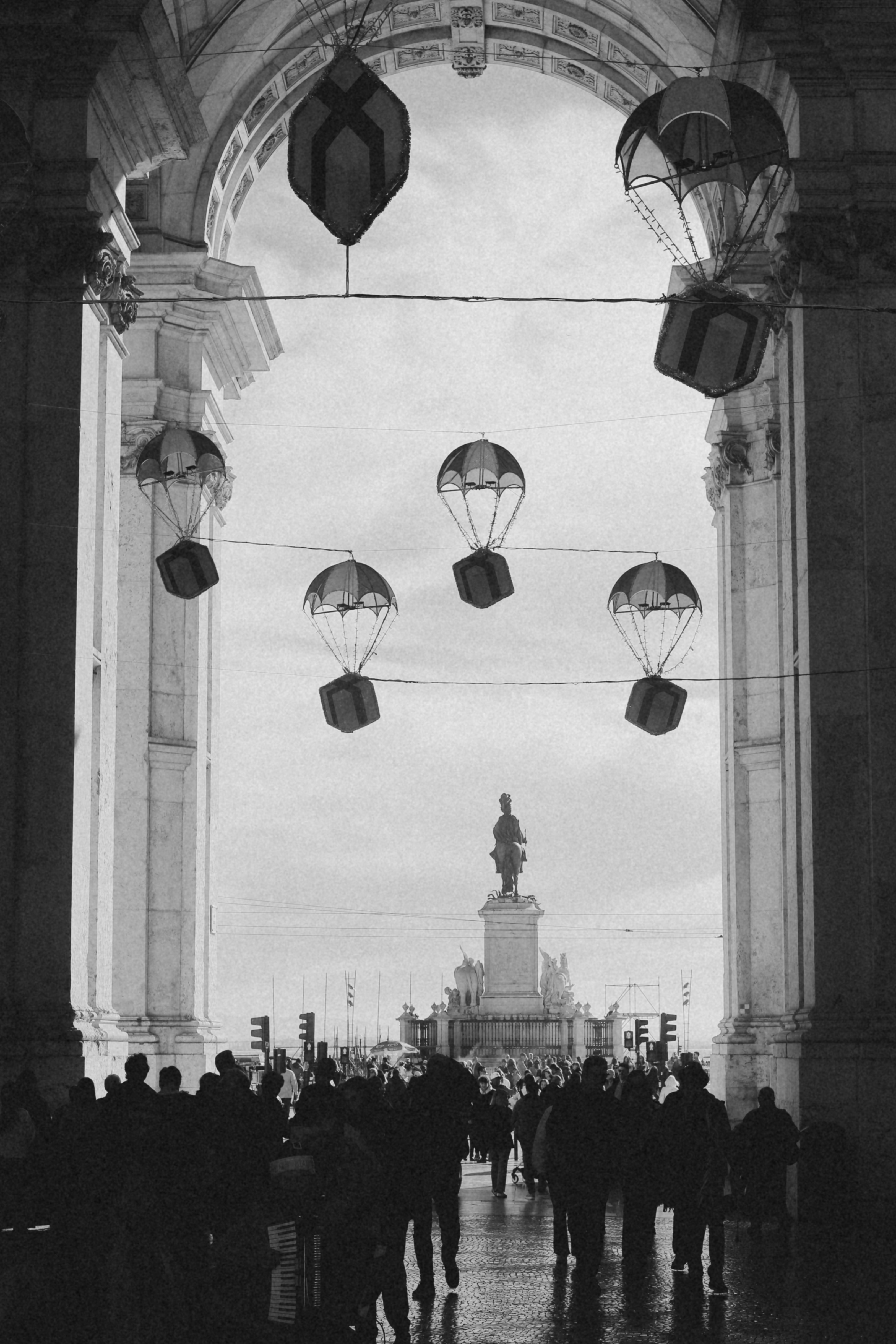 A crowd of people walking under hanging parachutes in a stone archway