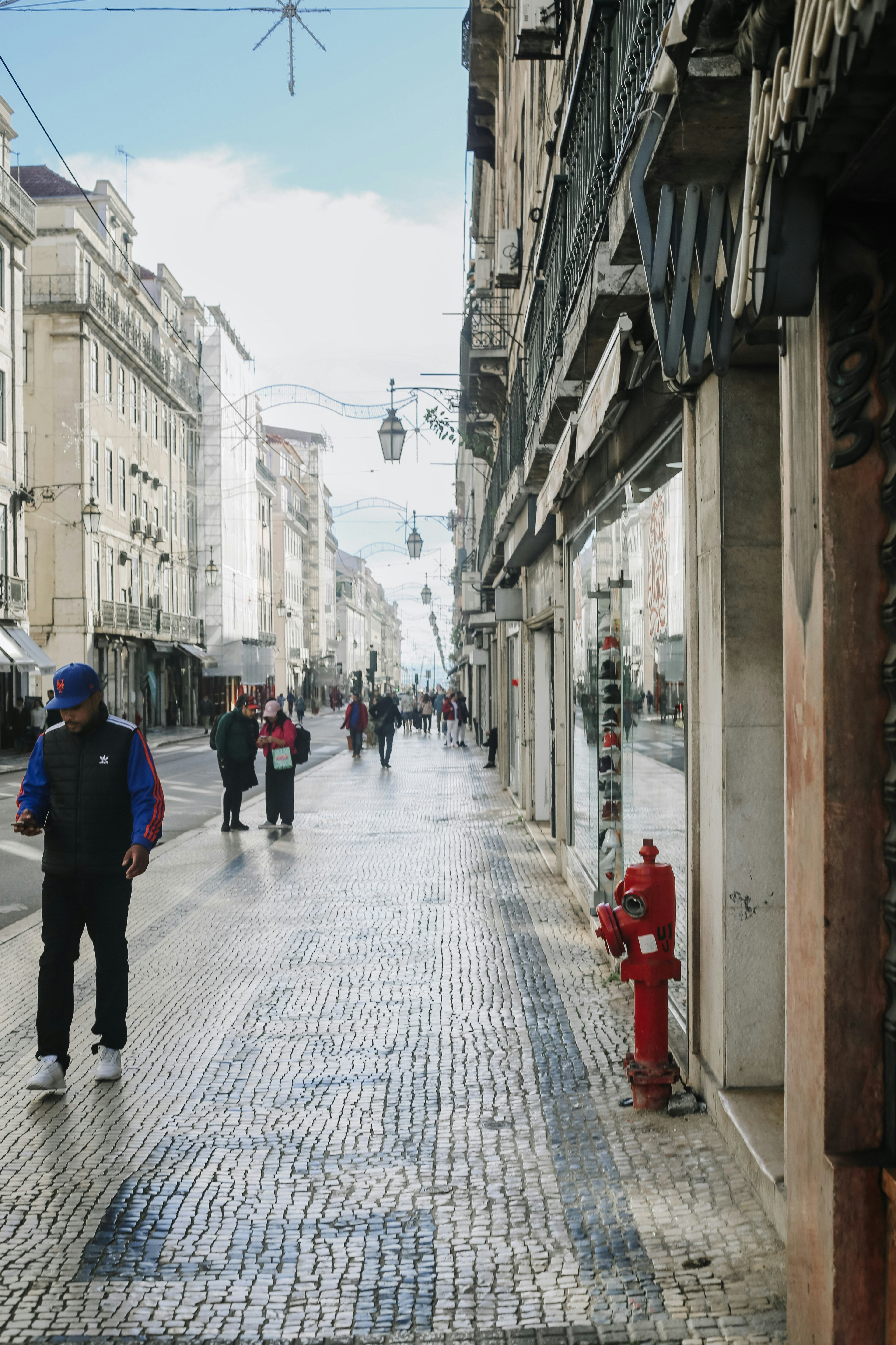 A person walking on a cobblestone street in Lisbon with a red fire hydrant
