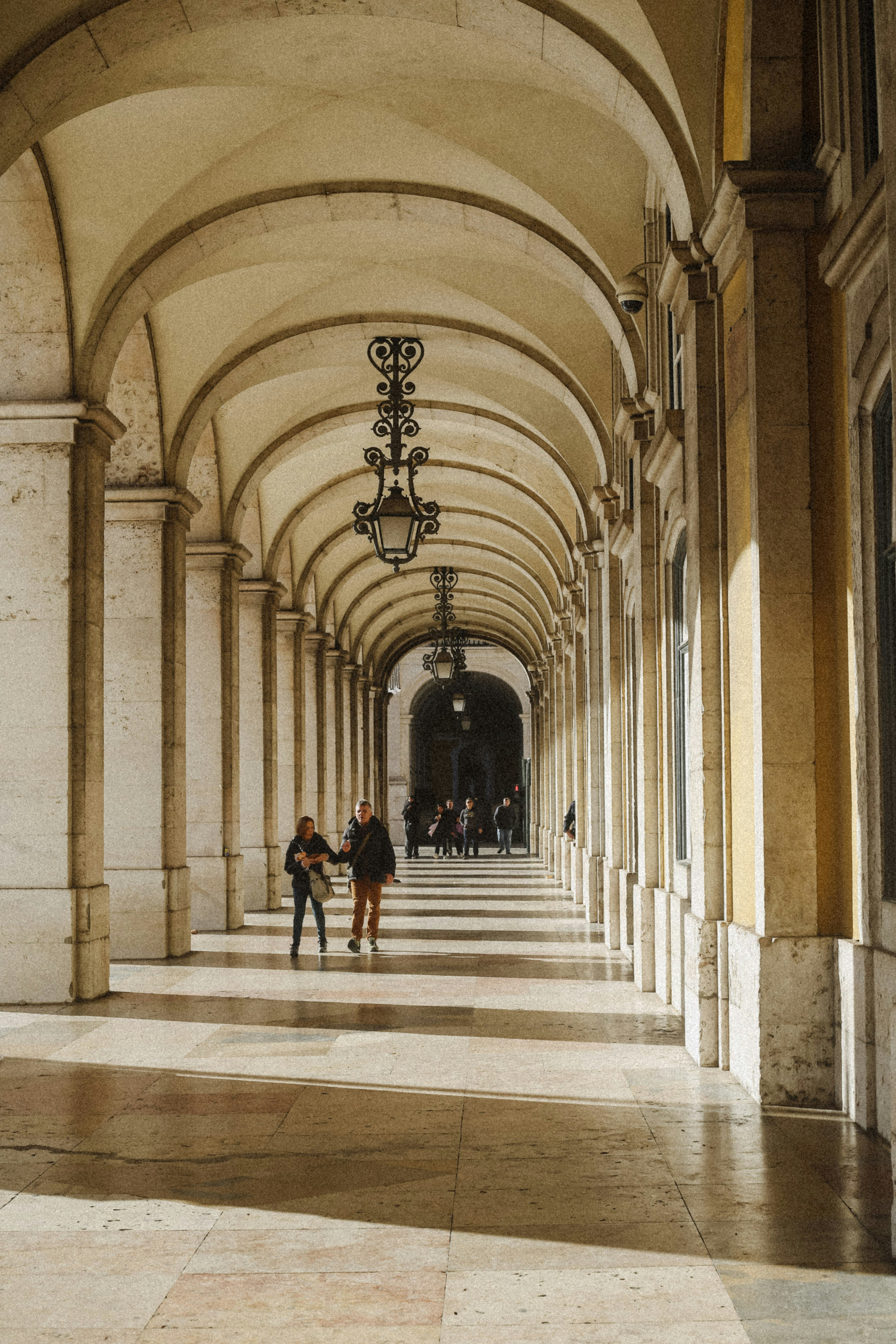 People walking through a long stone arched corridor with hanging lanterns