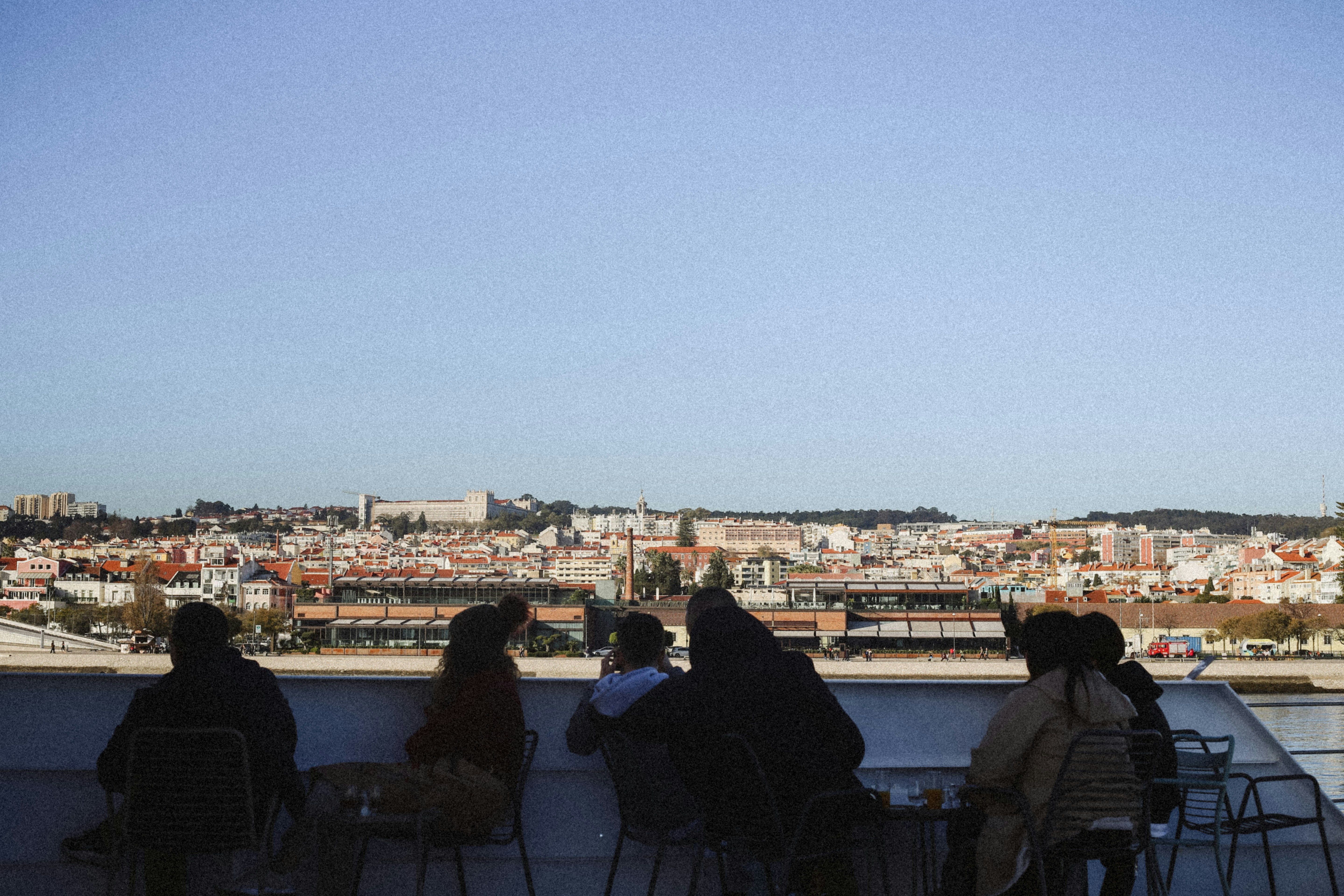 People sitting at tables on a boat deck overlooking the Lisbon cityscape