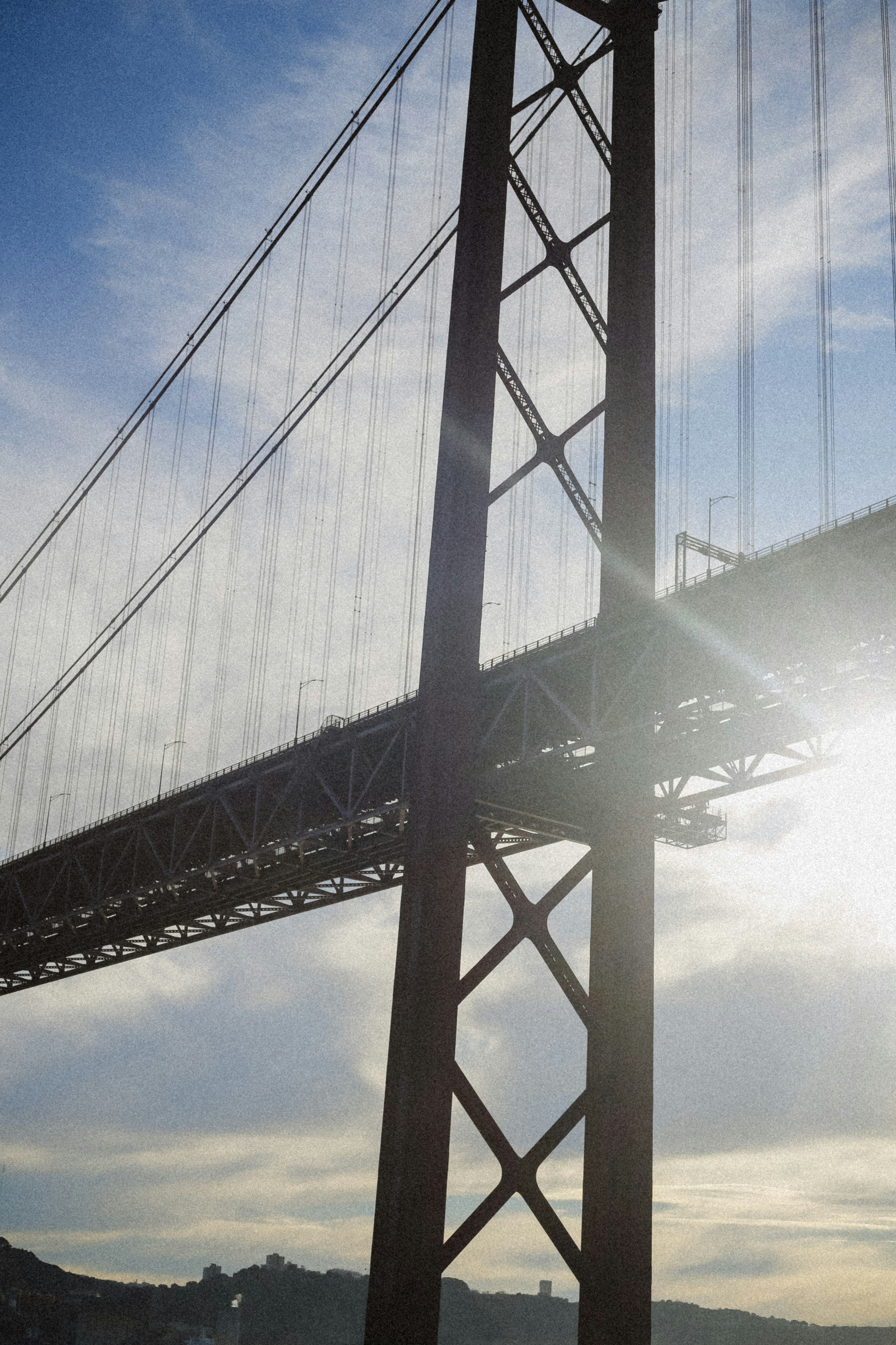 A large steel suspension bridge tower against a bright sky with low sun