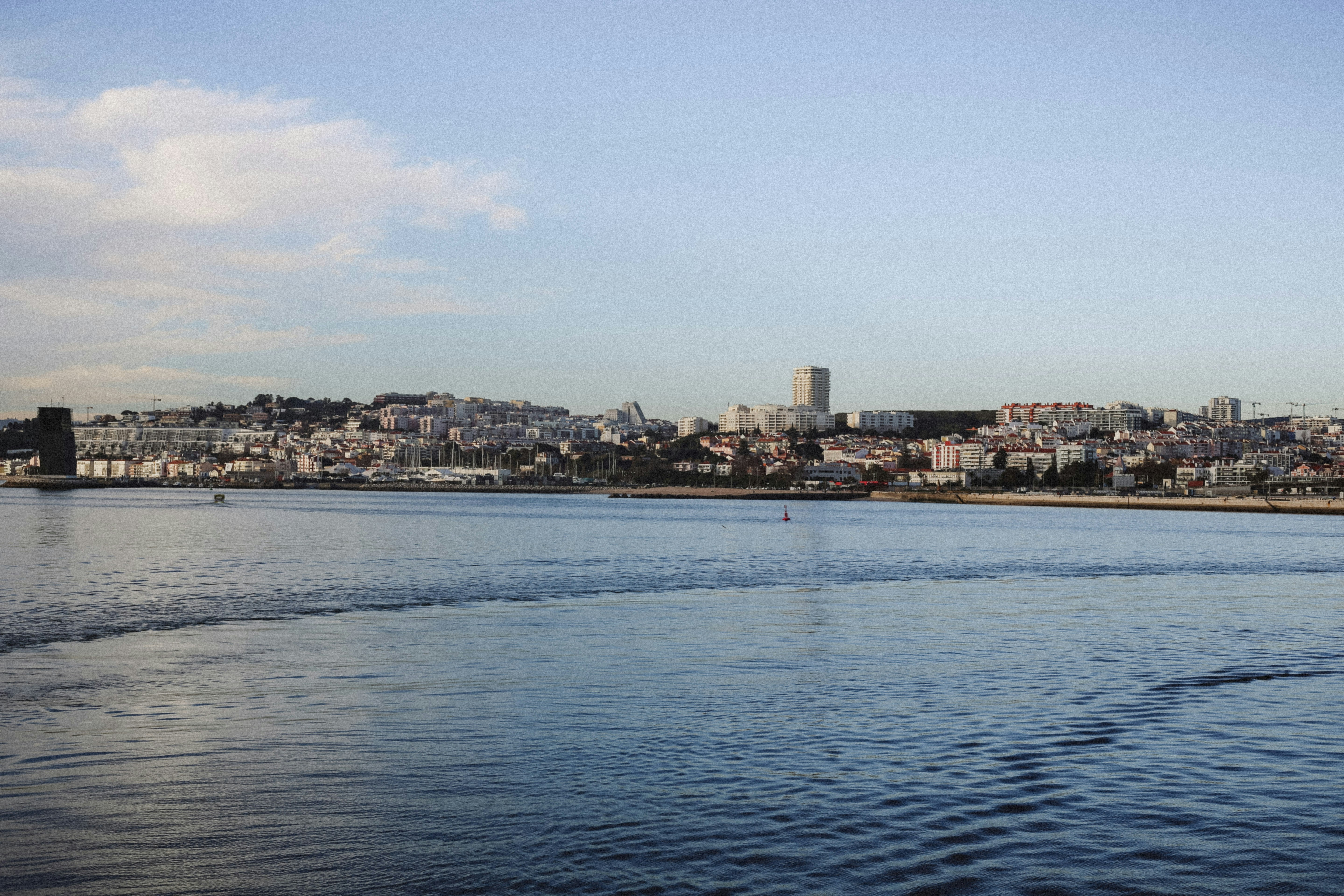 A view of the Lisbon waterfront with buildings and a marina under a clear sky