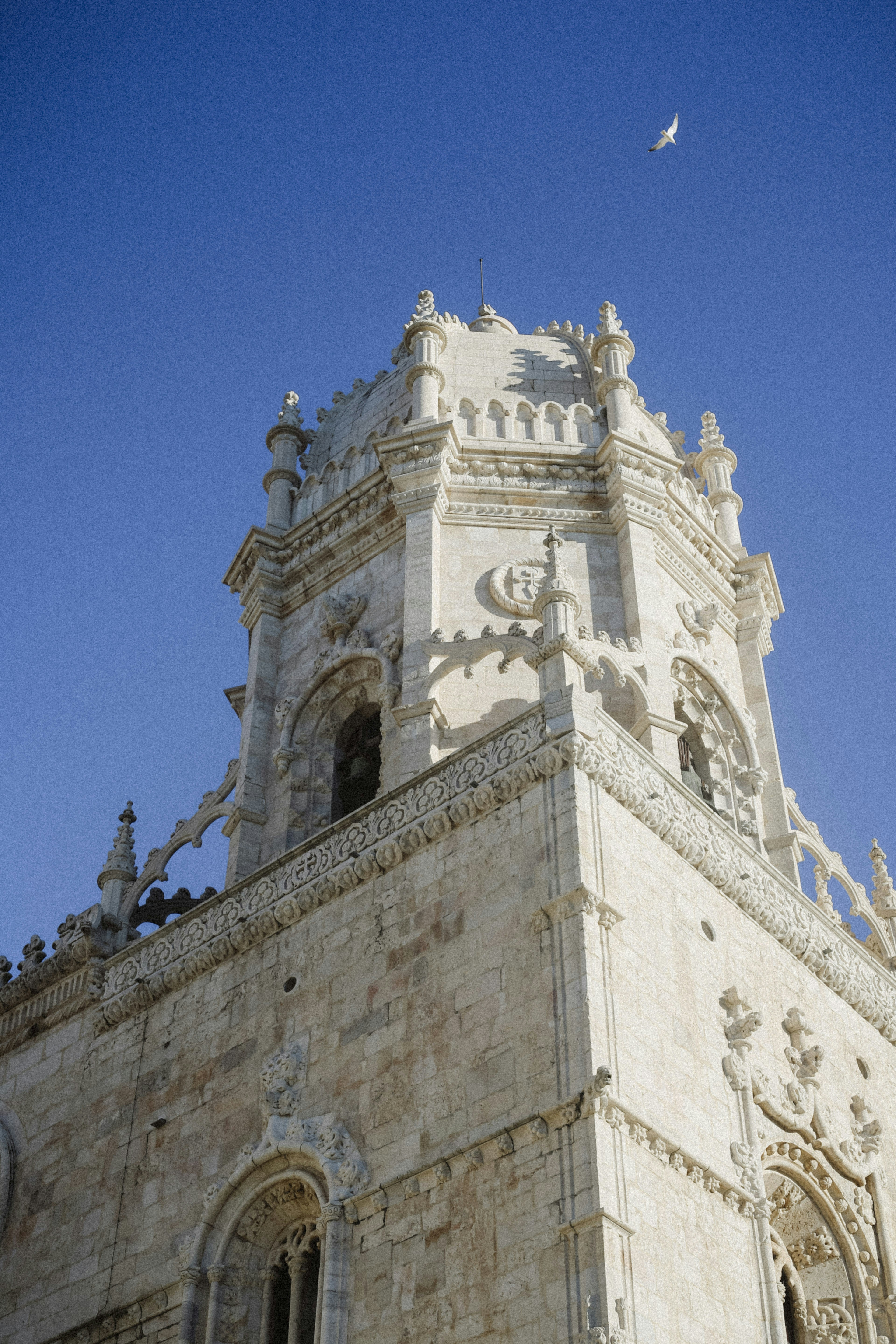The ornate stone bell tower of Jerónimos Monastery in Lisbon against a clear blue sky