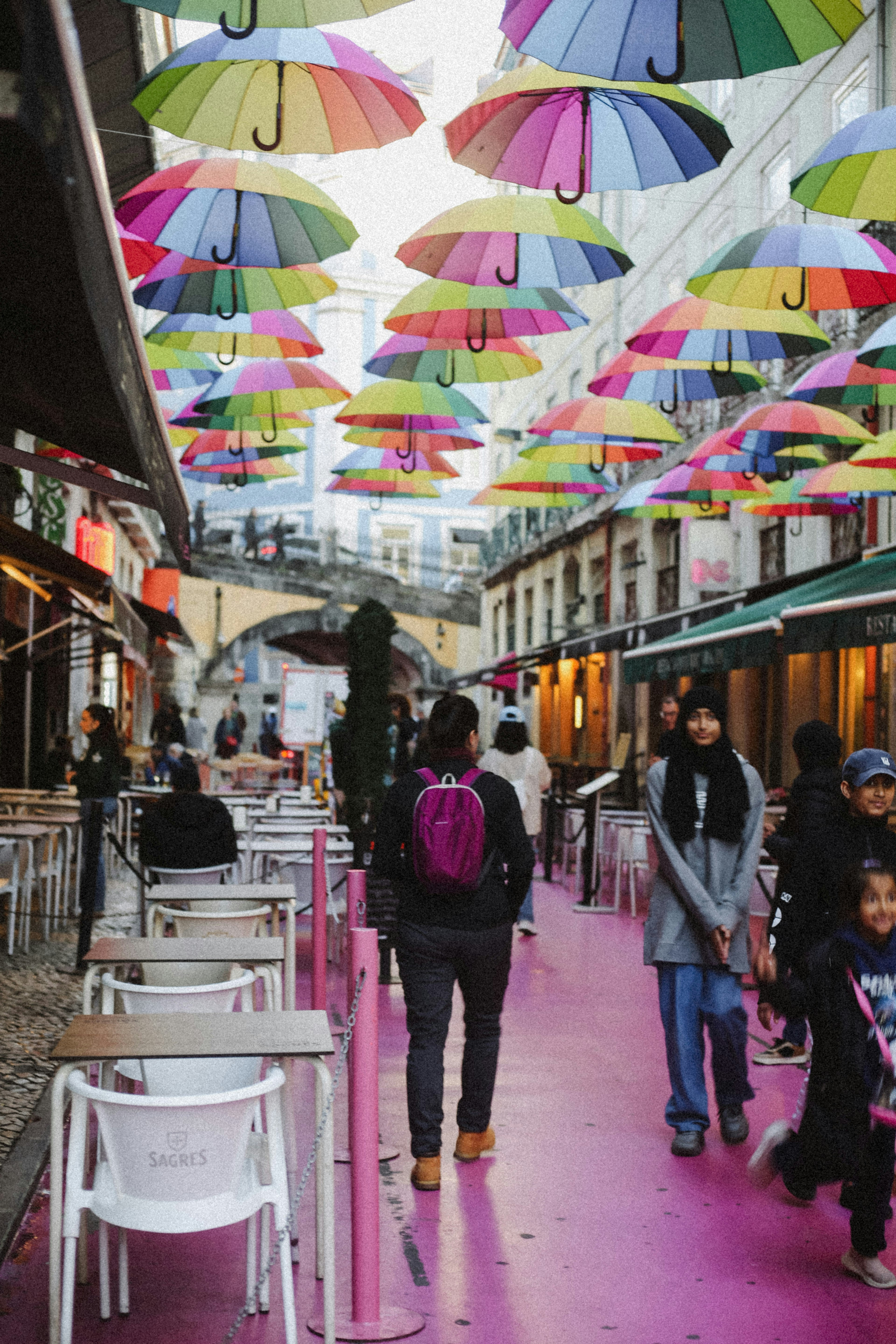 People walking on a pink street under a canopy of colorful umbrellas in Lisbon