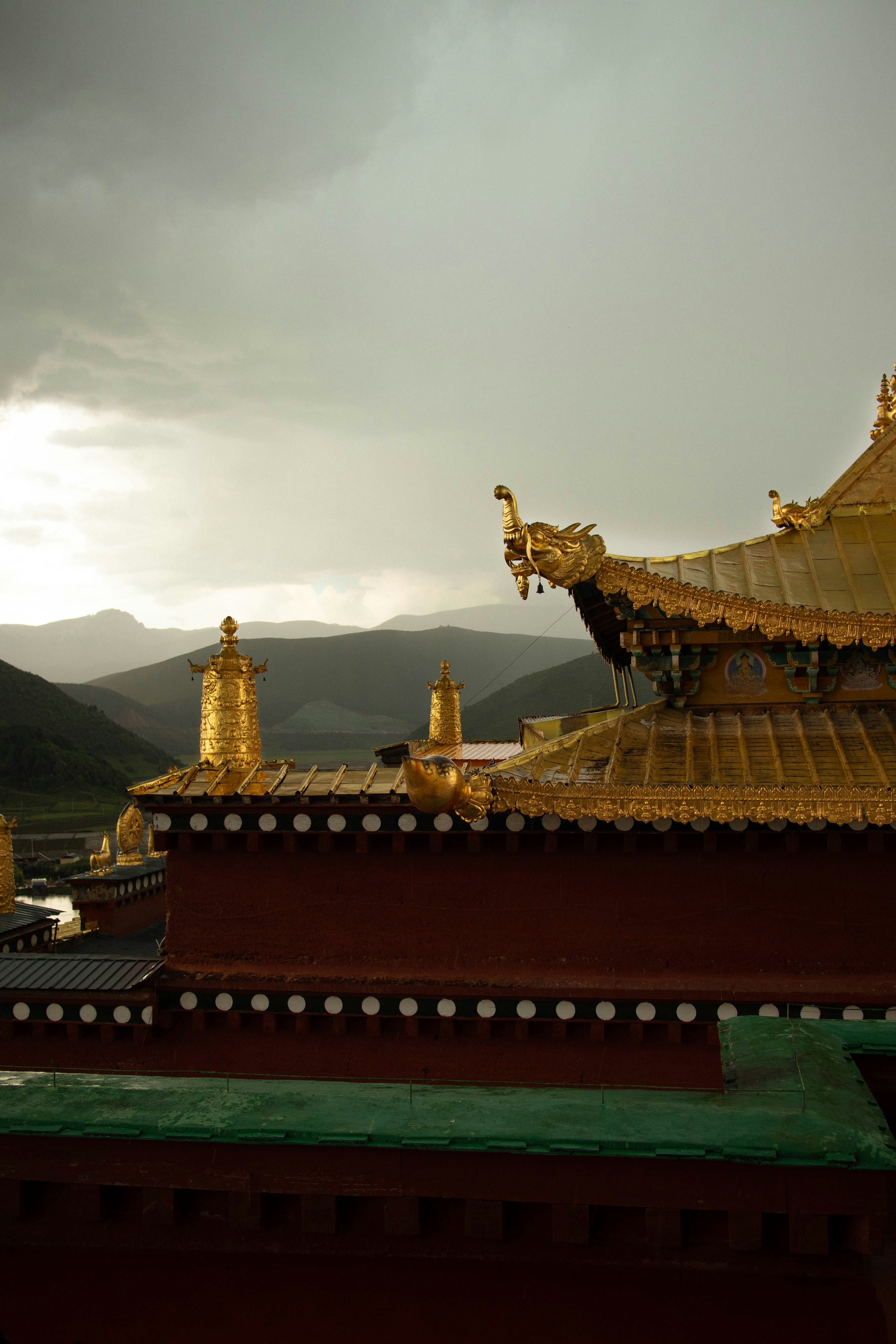 Golden roof ornaments on a red temple building against a backdrop of mountains
