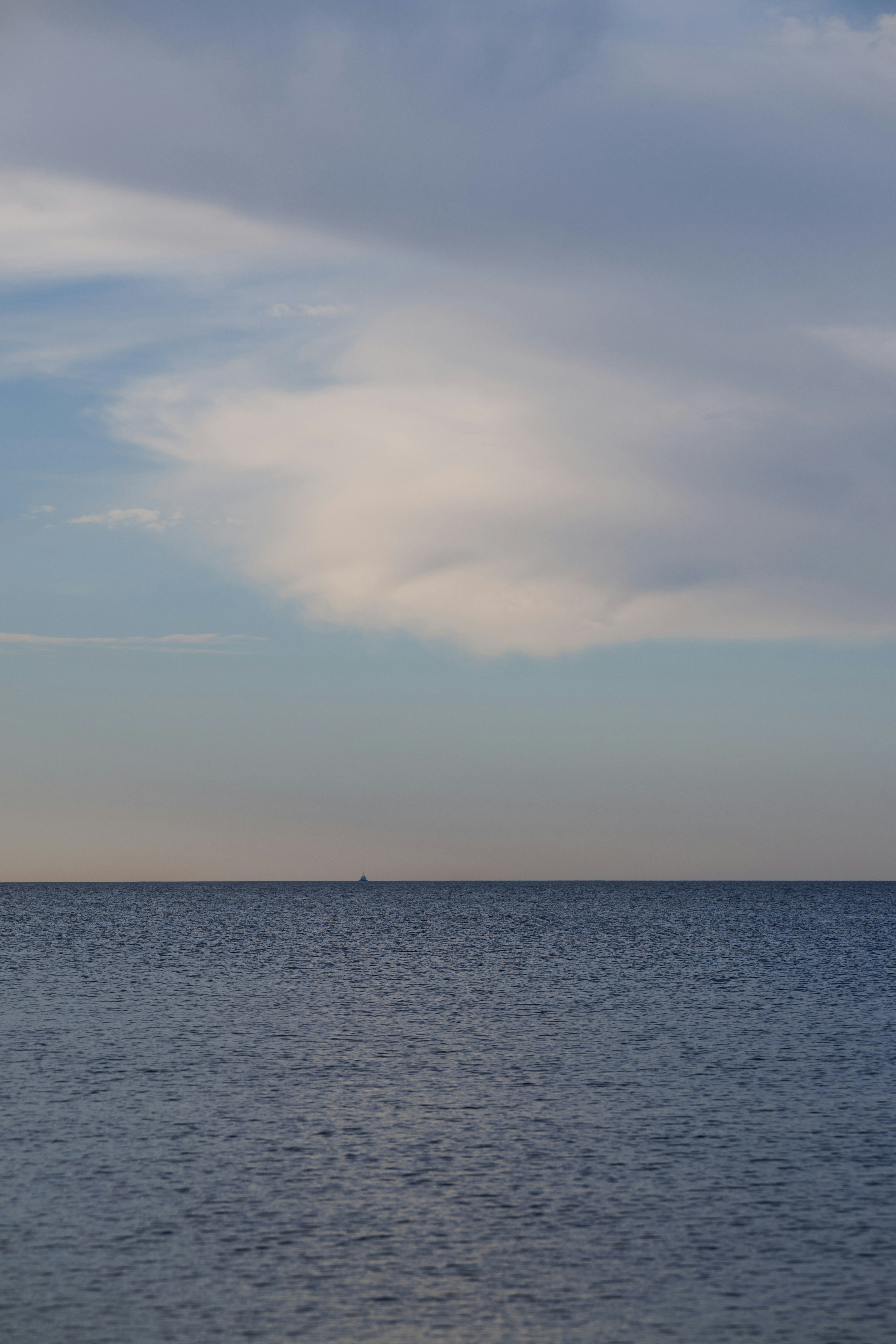Un petit bateau à l’horizon lointain sous un vaste ciel nuageux