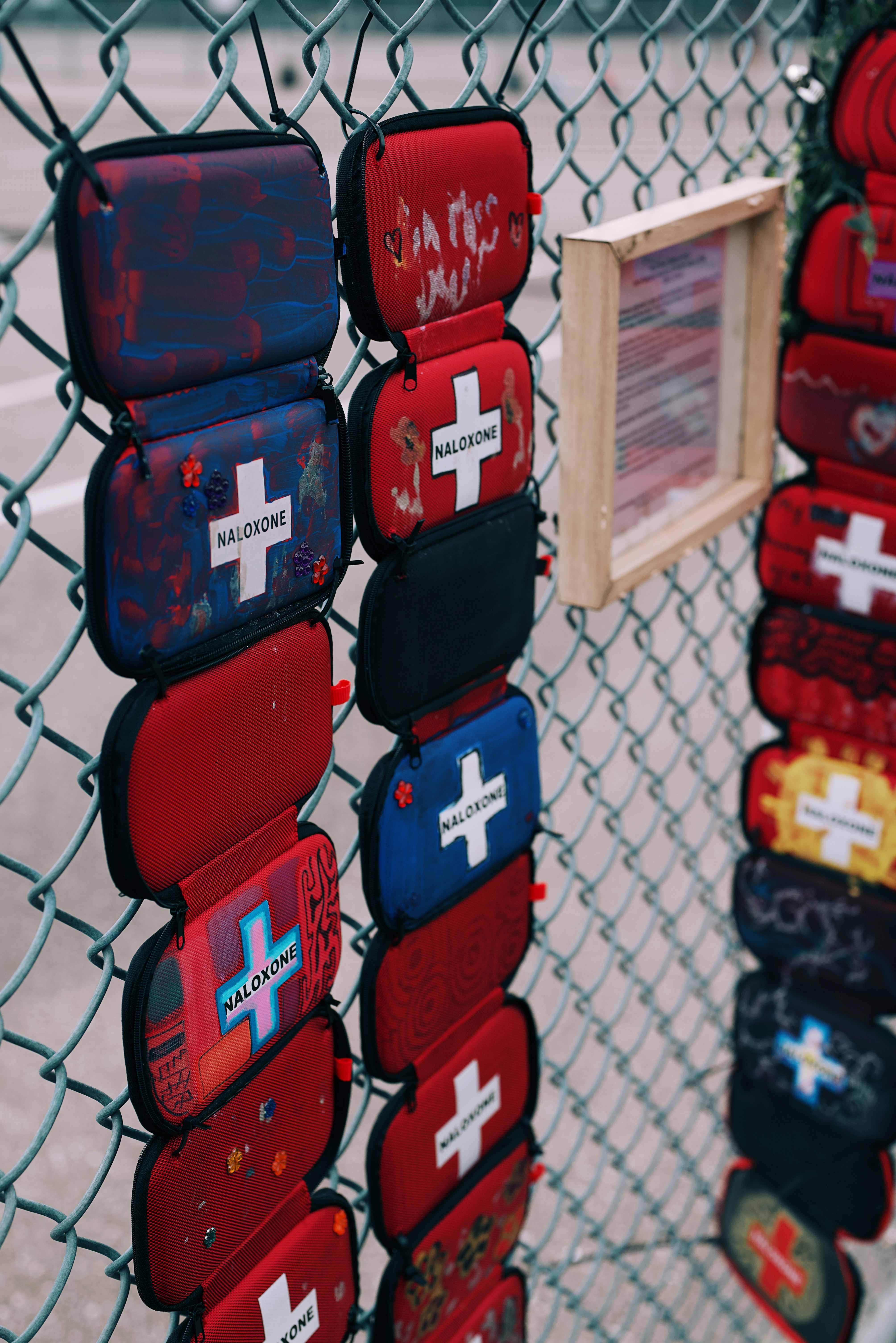 De petites pochettes rouges et bleues à fermeture éclair, étiquetées Naloxone, suspendues à une clôture en chaîne