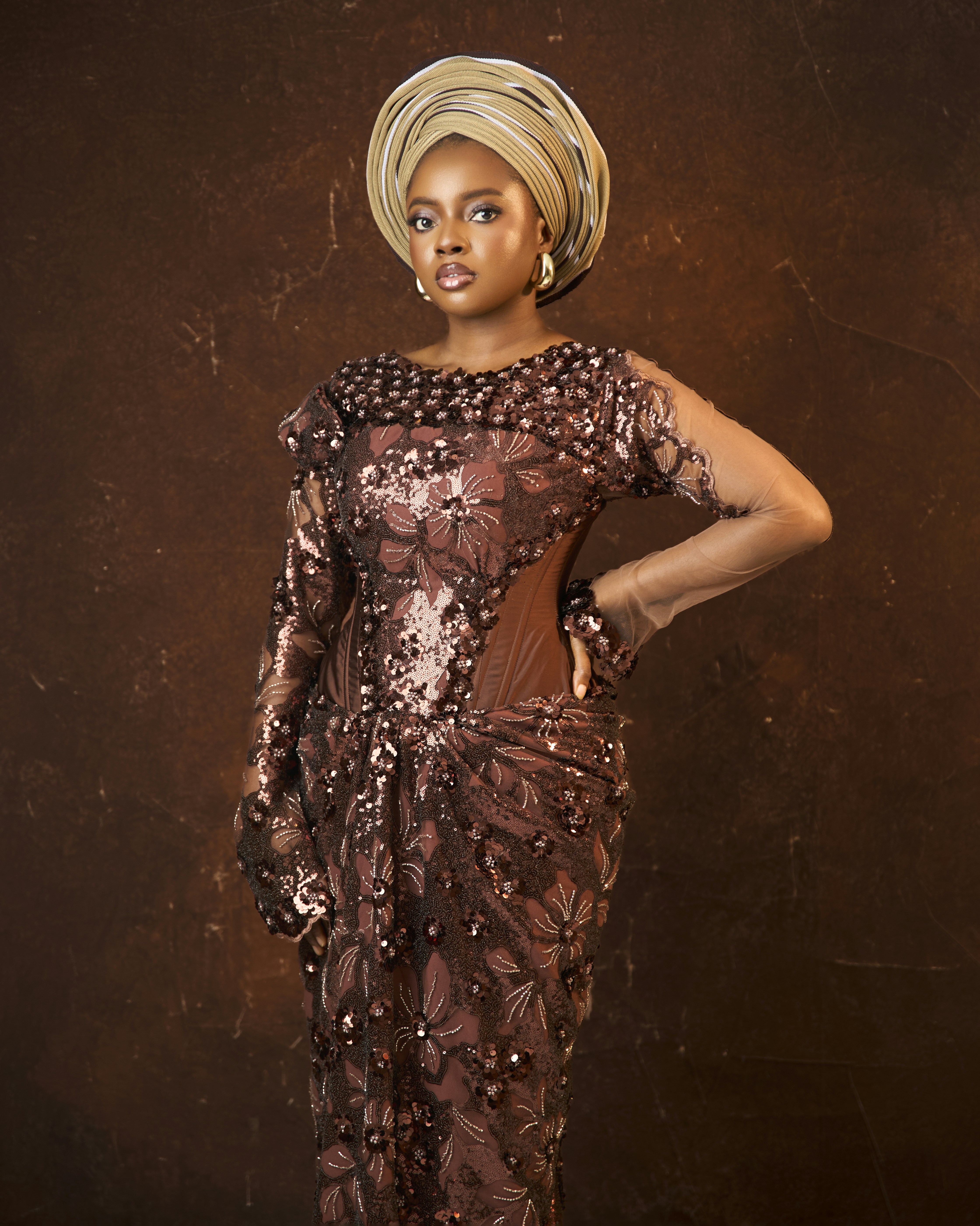 A woman wearing a brown sequined dress and a matching headwrap against a brown background