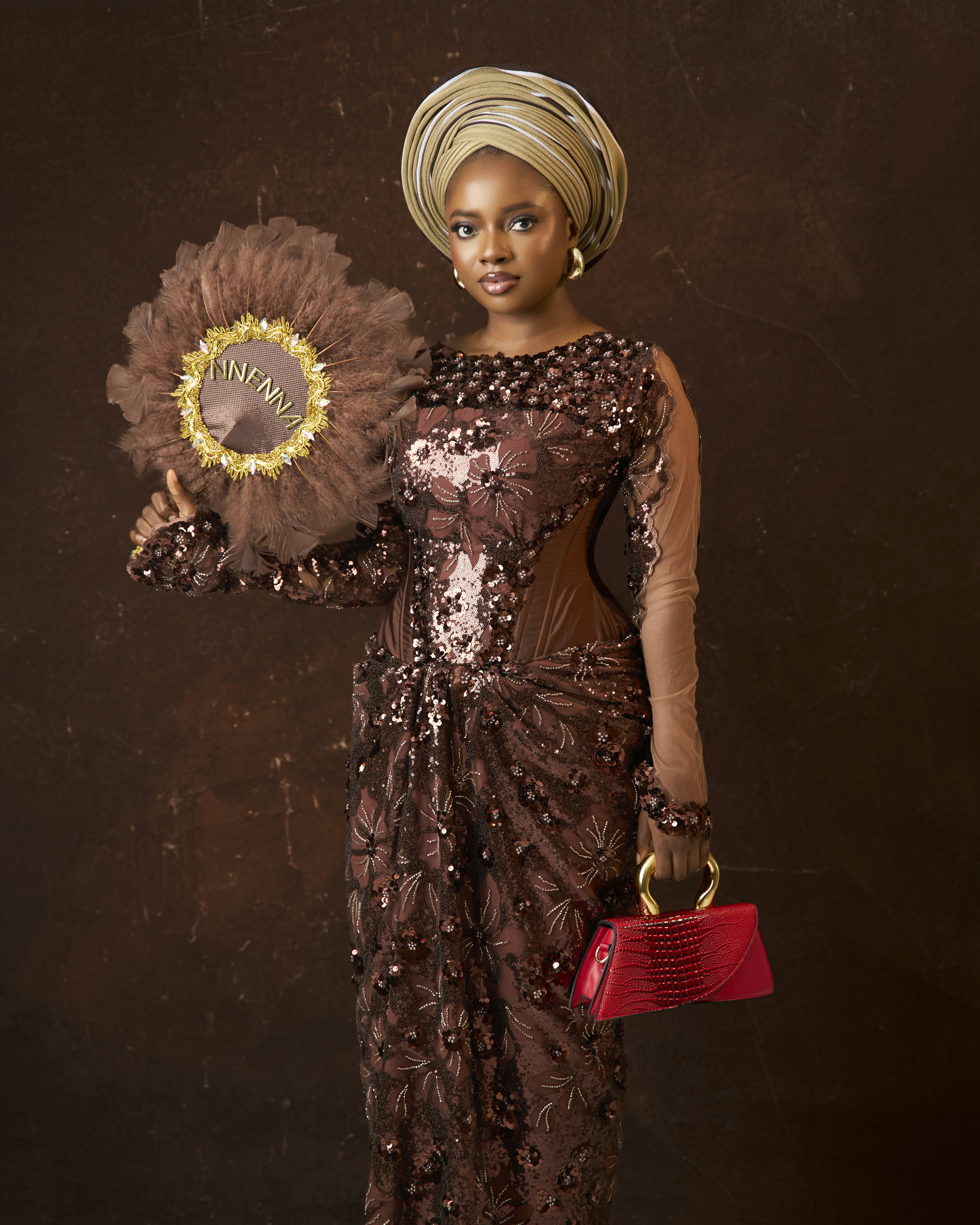 A woman in a sequined brown dress and headwrap holding a feathered fan