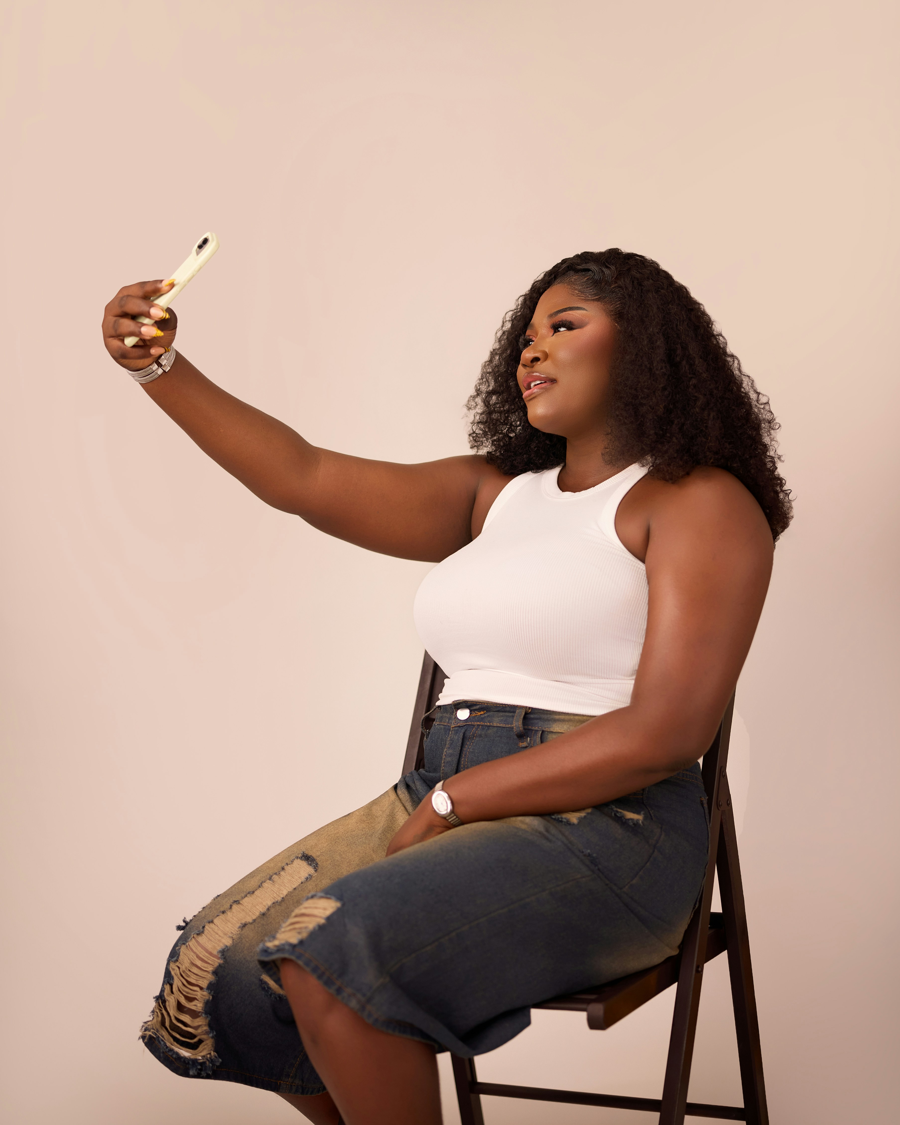 A woman in a white tank top and distressed jeans taking a selfie