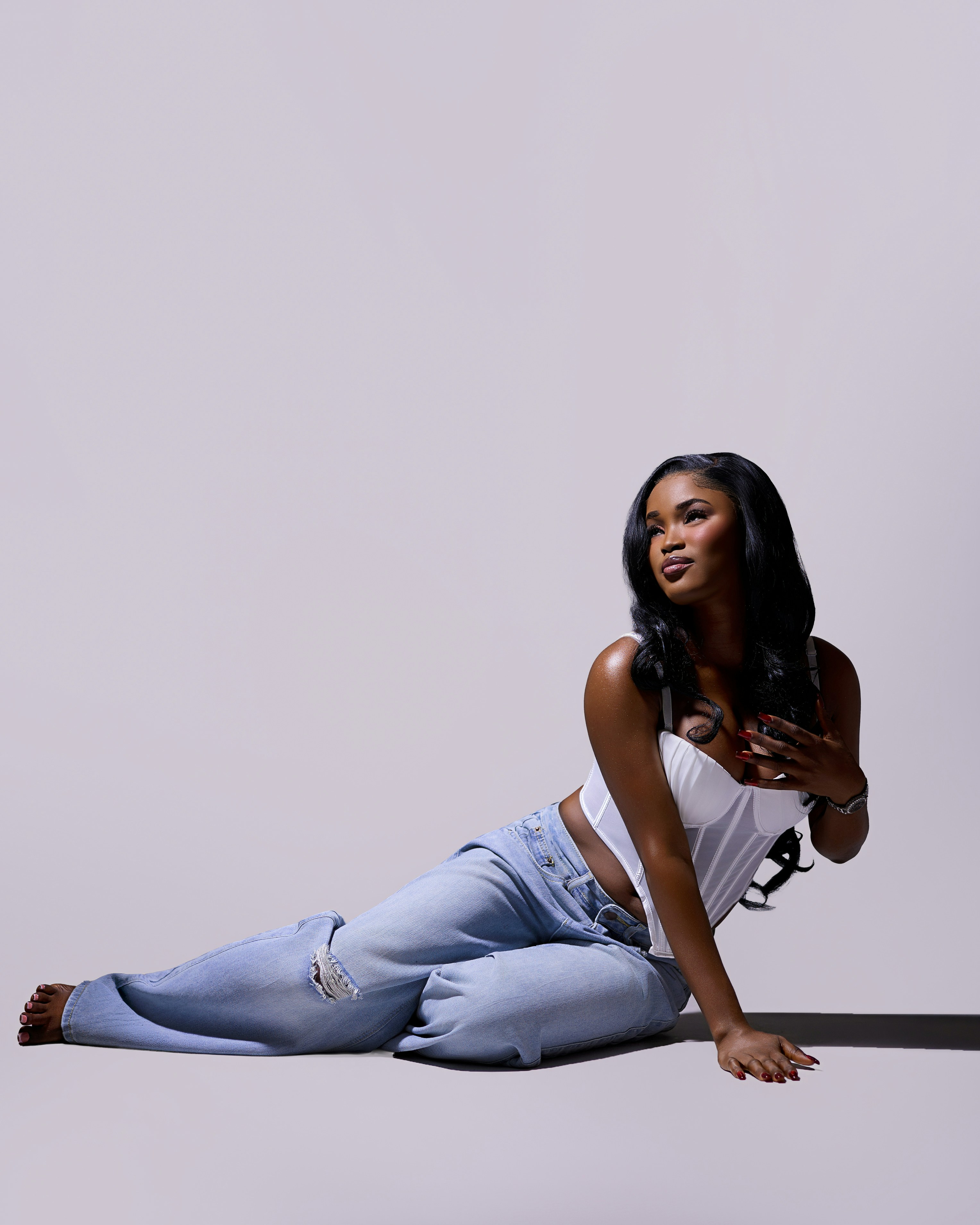 A woman in a white corset top and blue jeans sitting on the floor