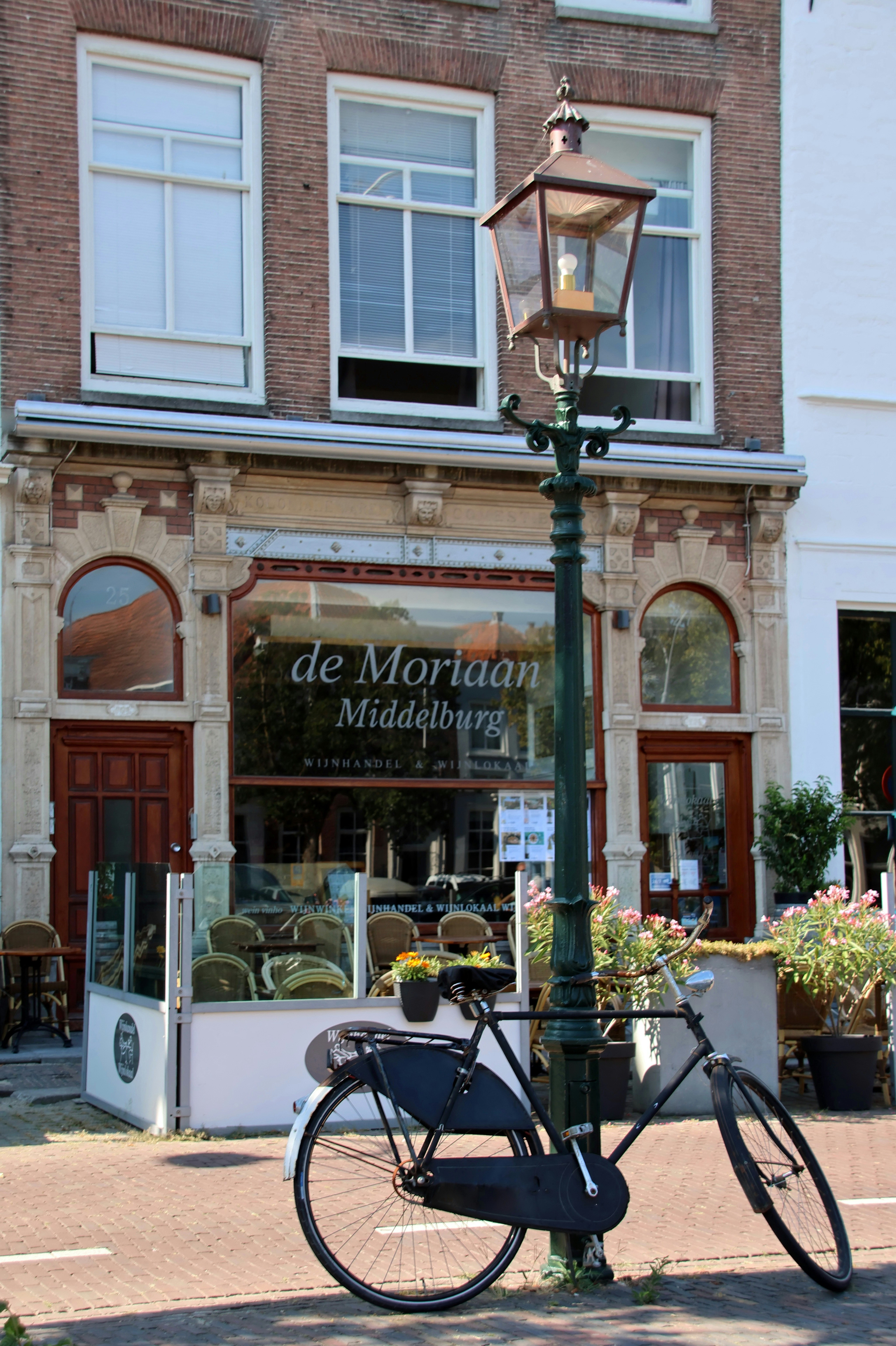 A black bicycle beside a vintage green lamppost outside a brick storefront