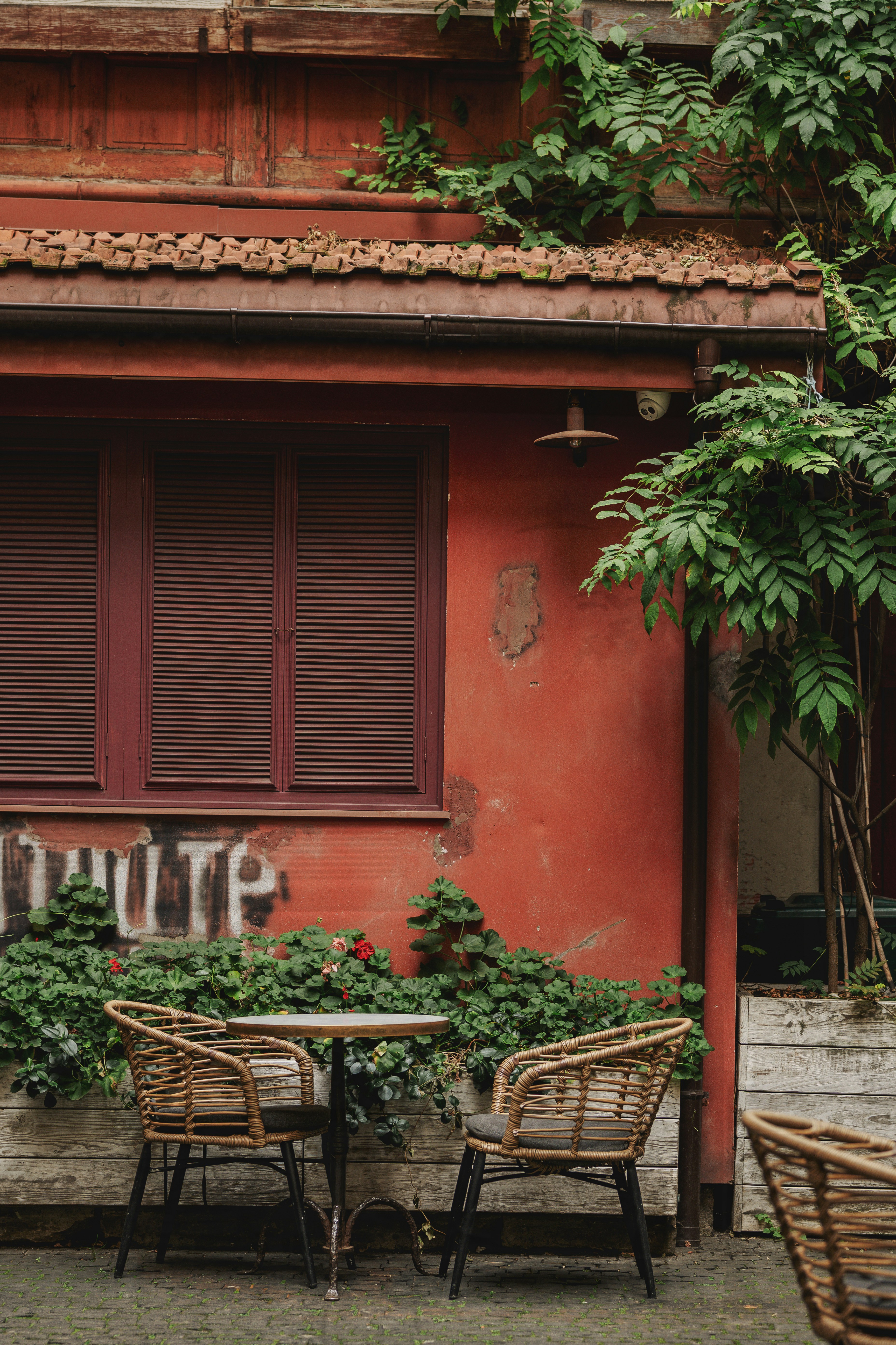 Two wicker chairs and a small table against a weathered red wall