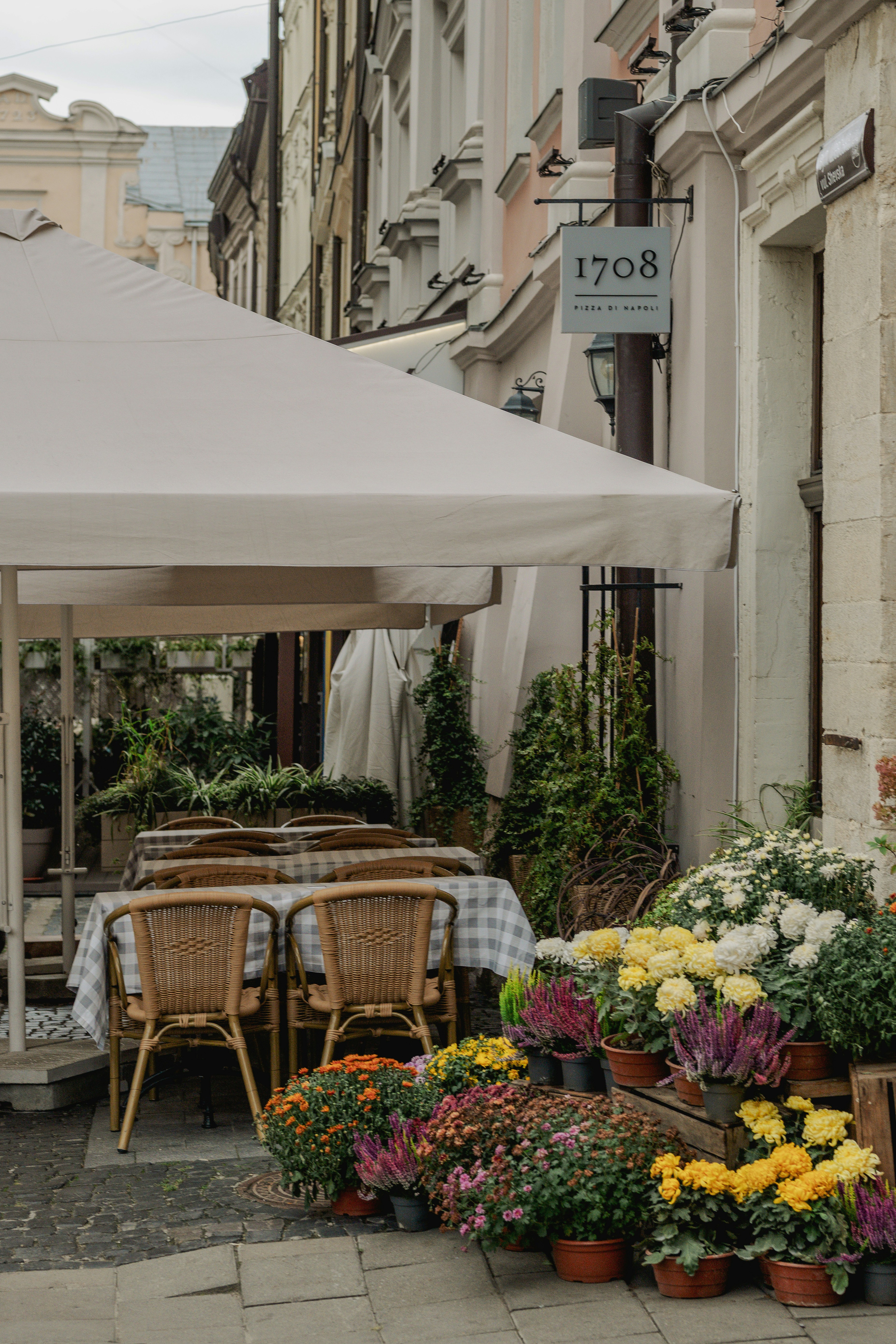 Outdoor restaurant seating with wicker chairs and checkered tablecloths under a large beige umbrella