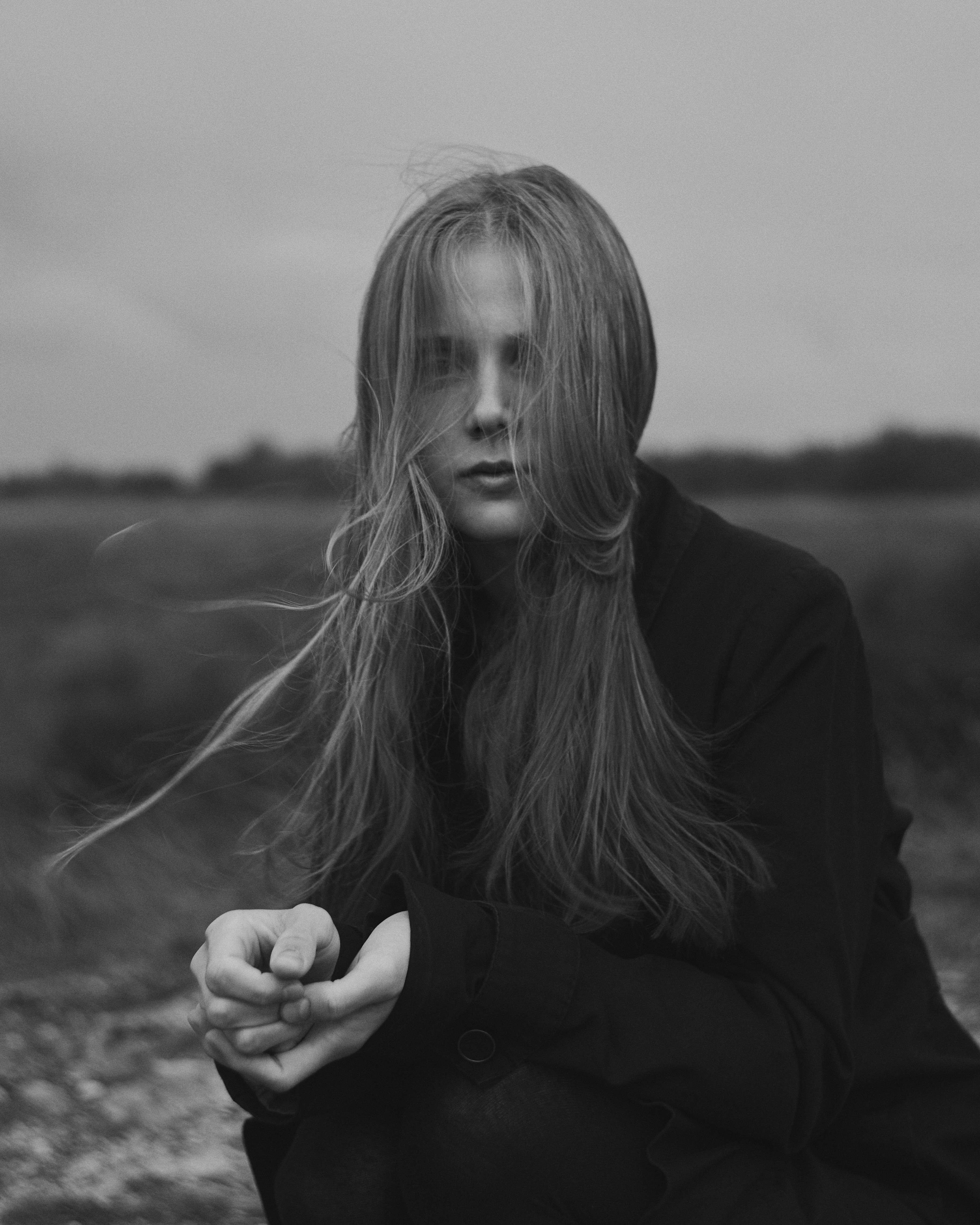 A person with long hair blowing in the wind in a dark coat