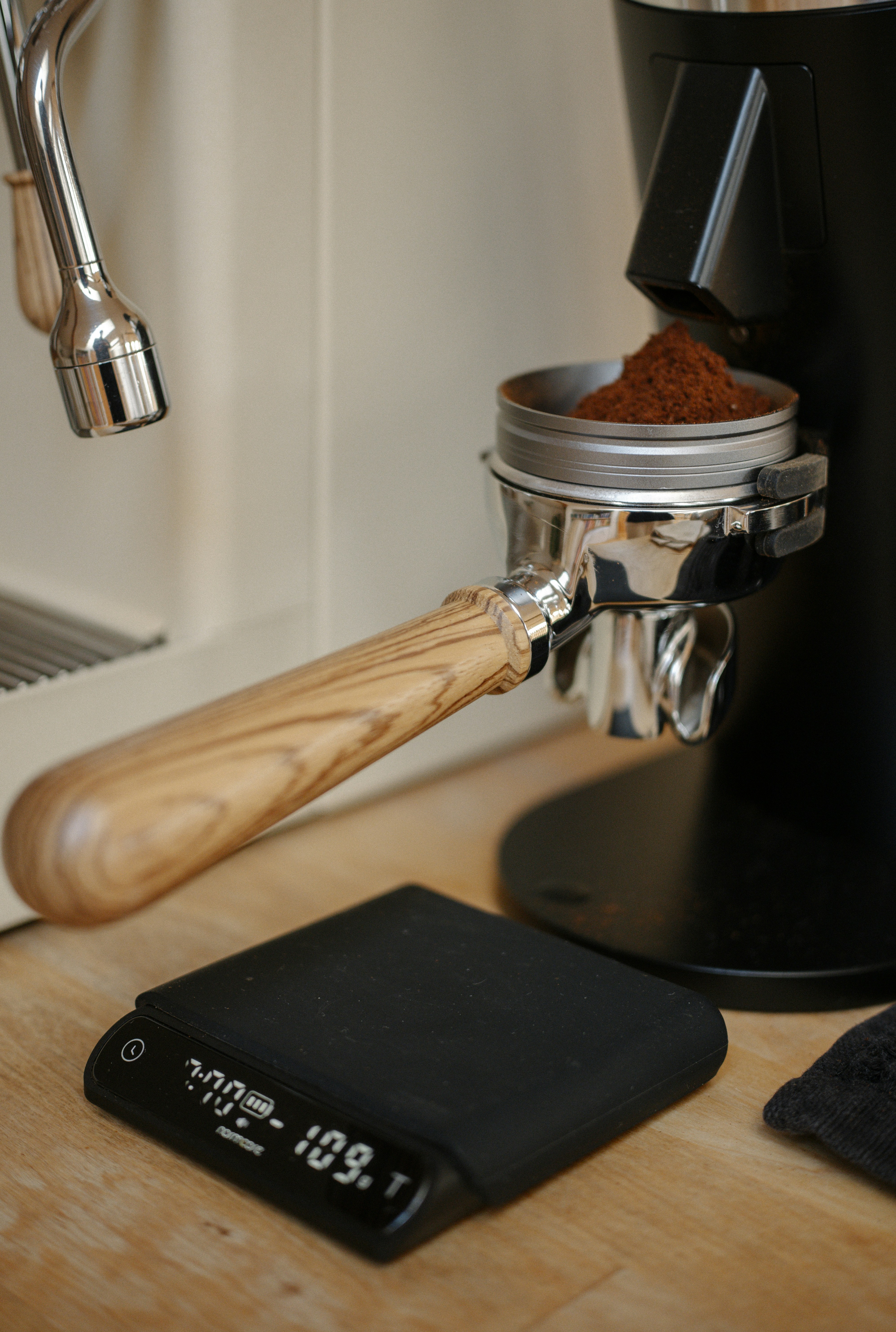 Ein Siebträger mit einem Holzgriff, gefüllt mit Kaffeesatz auf digitaler Waage, gefüllt mit Kaffeesatz