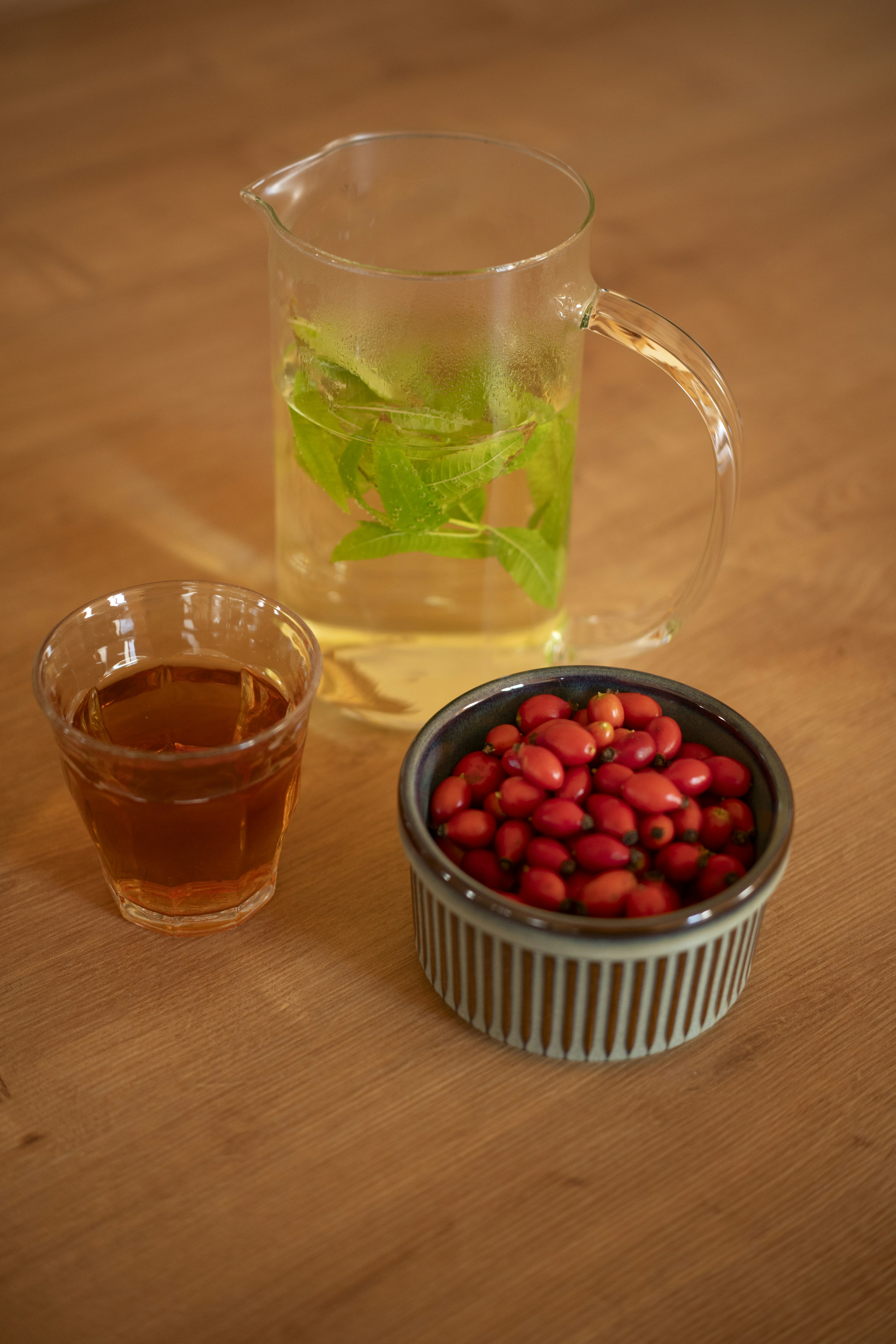 Ein Glaskanne mit Kräutertee, ein Glas Tee und Hagebutten in einer Schüssel