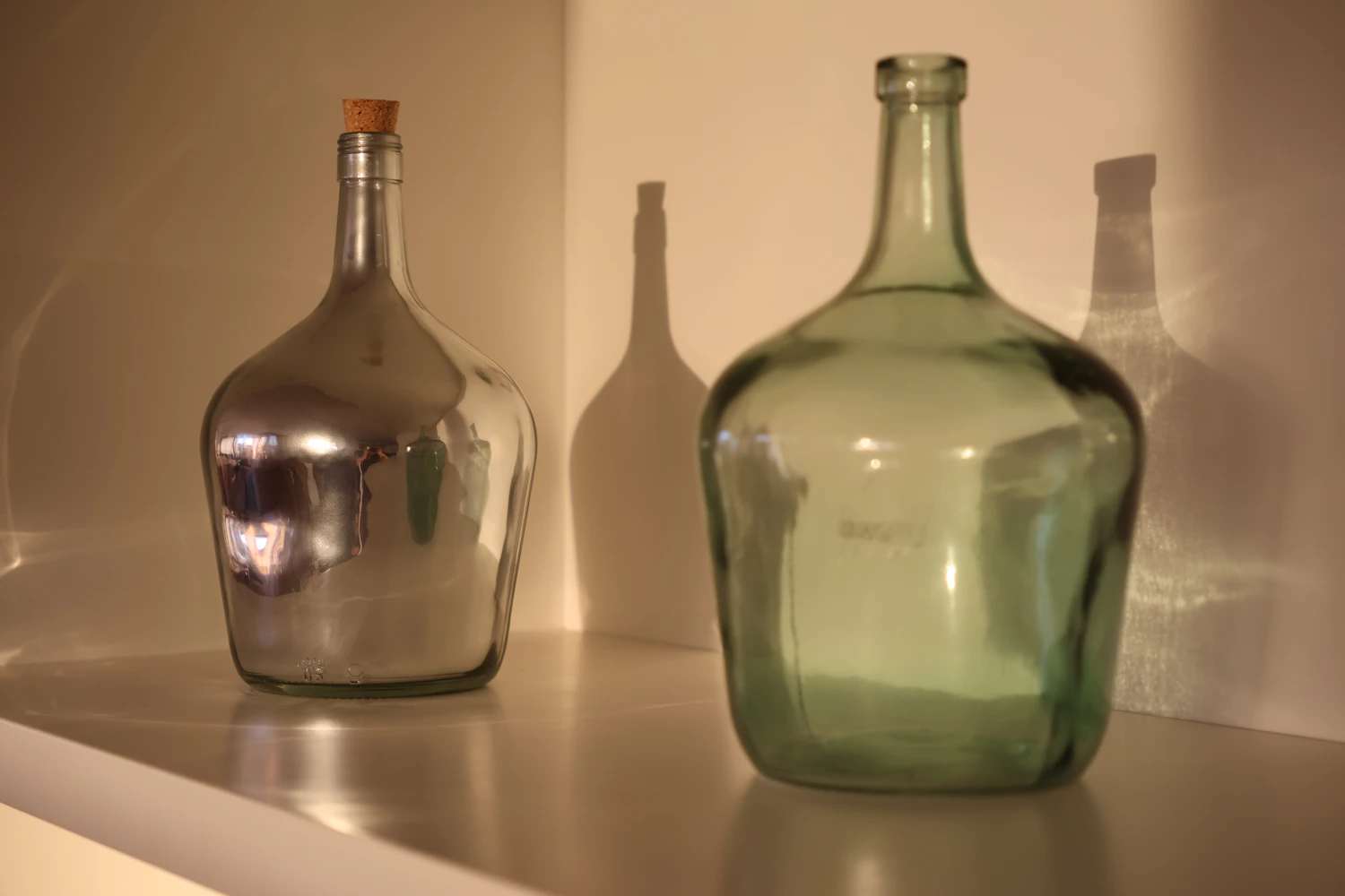 A silver and a green glass demijohn standing on a white counter