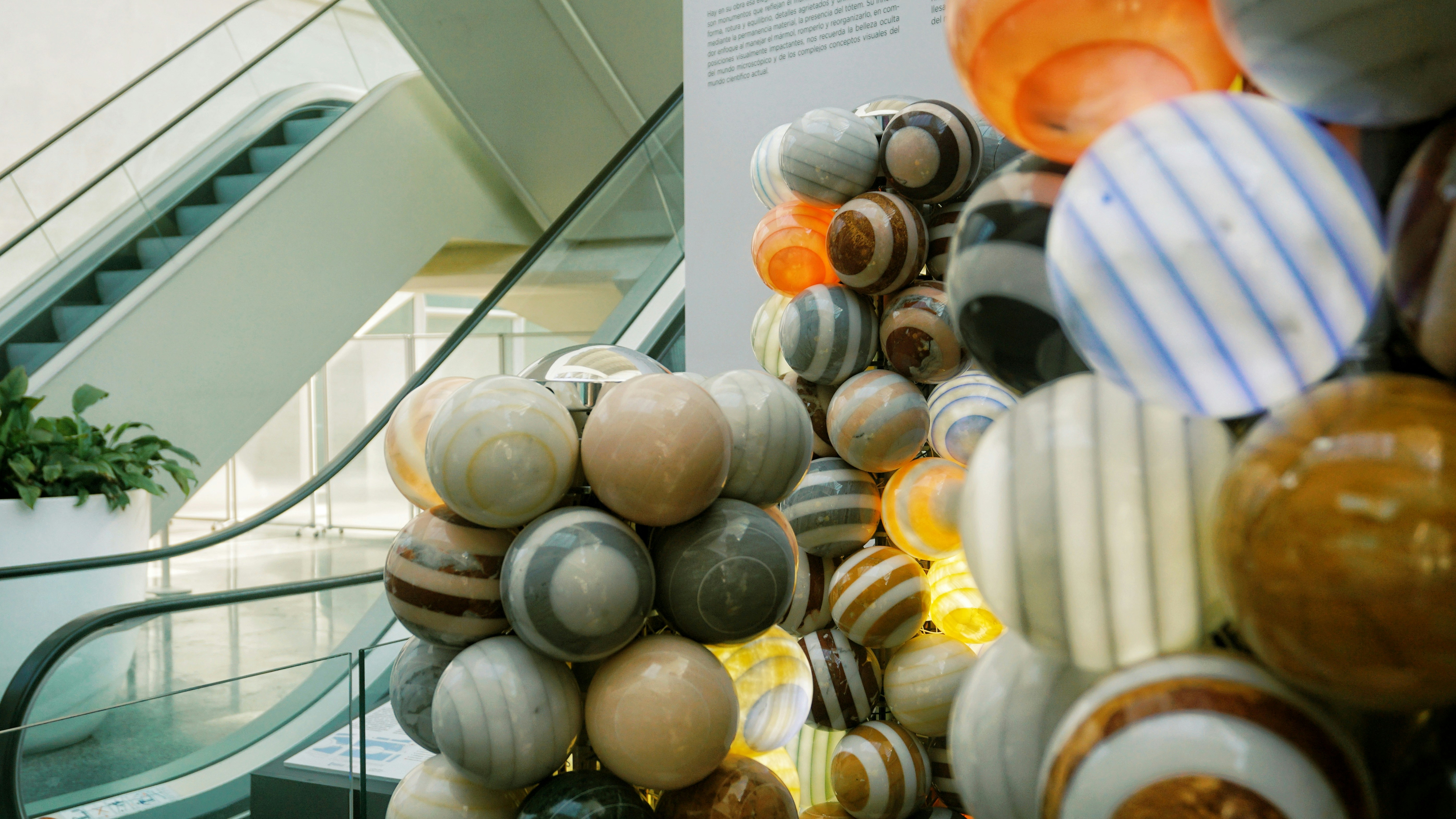 A sculpture of stacked glass spheres in an atrium with an escalator