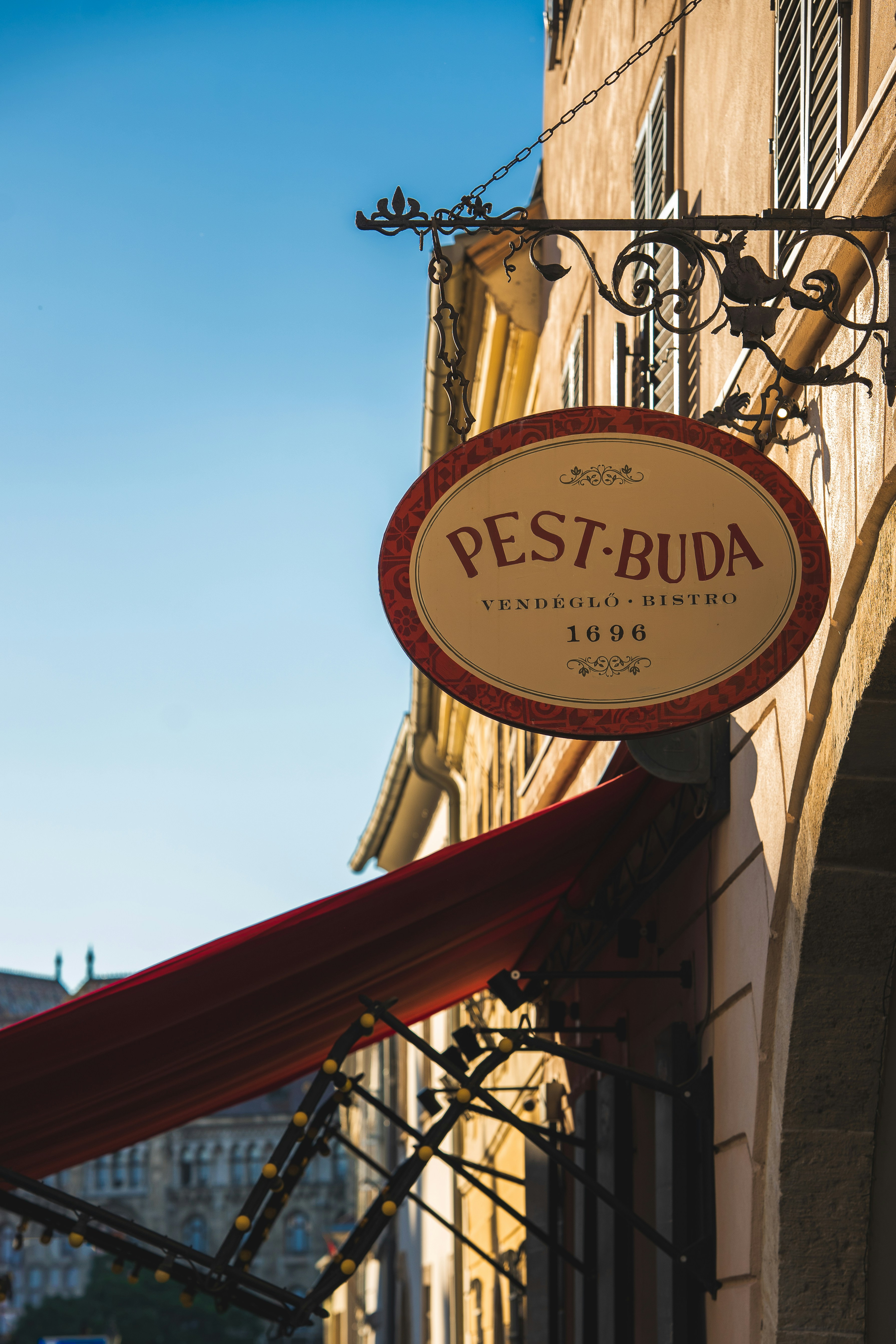 An oval sign reading Pest-Buda hanging from a wrought iron bracket on a building
