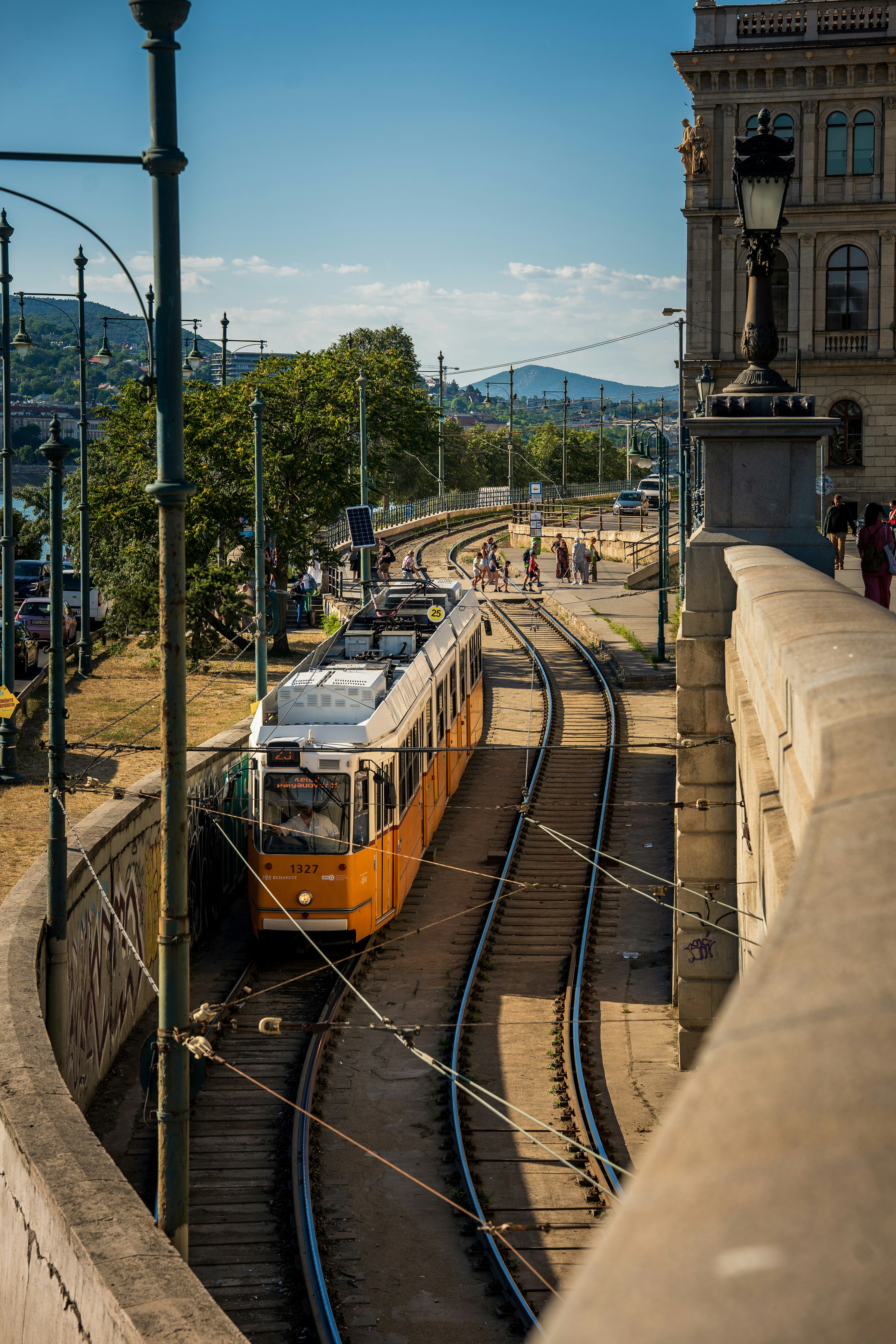 A yellow tram traveling along tracks beside a stone wall in Budapest