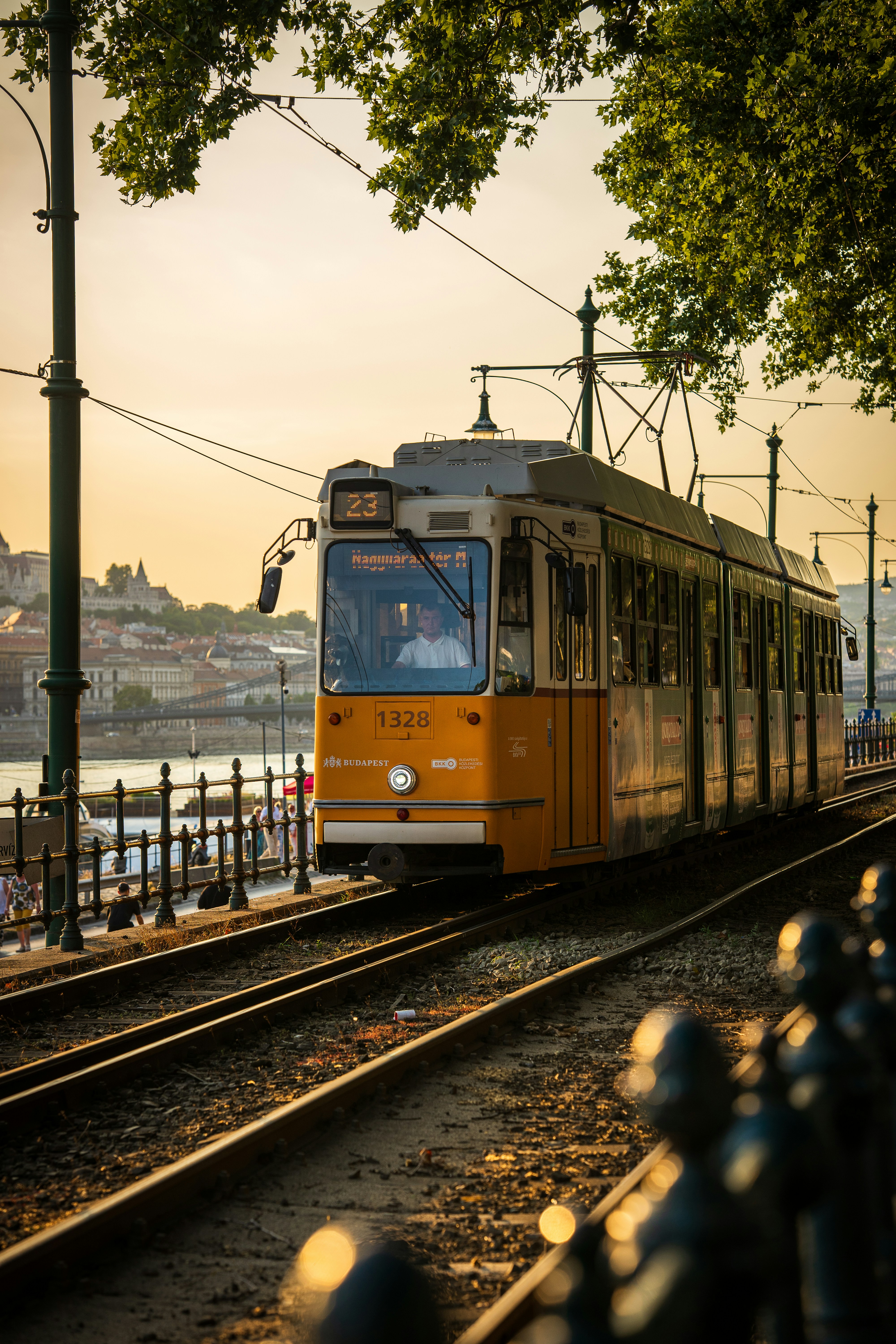 A yellow tram traveling along tracks by the Danube river in Budapest at sunset