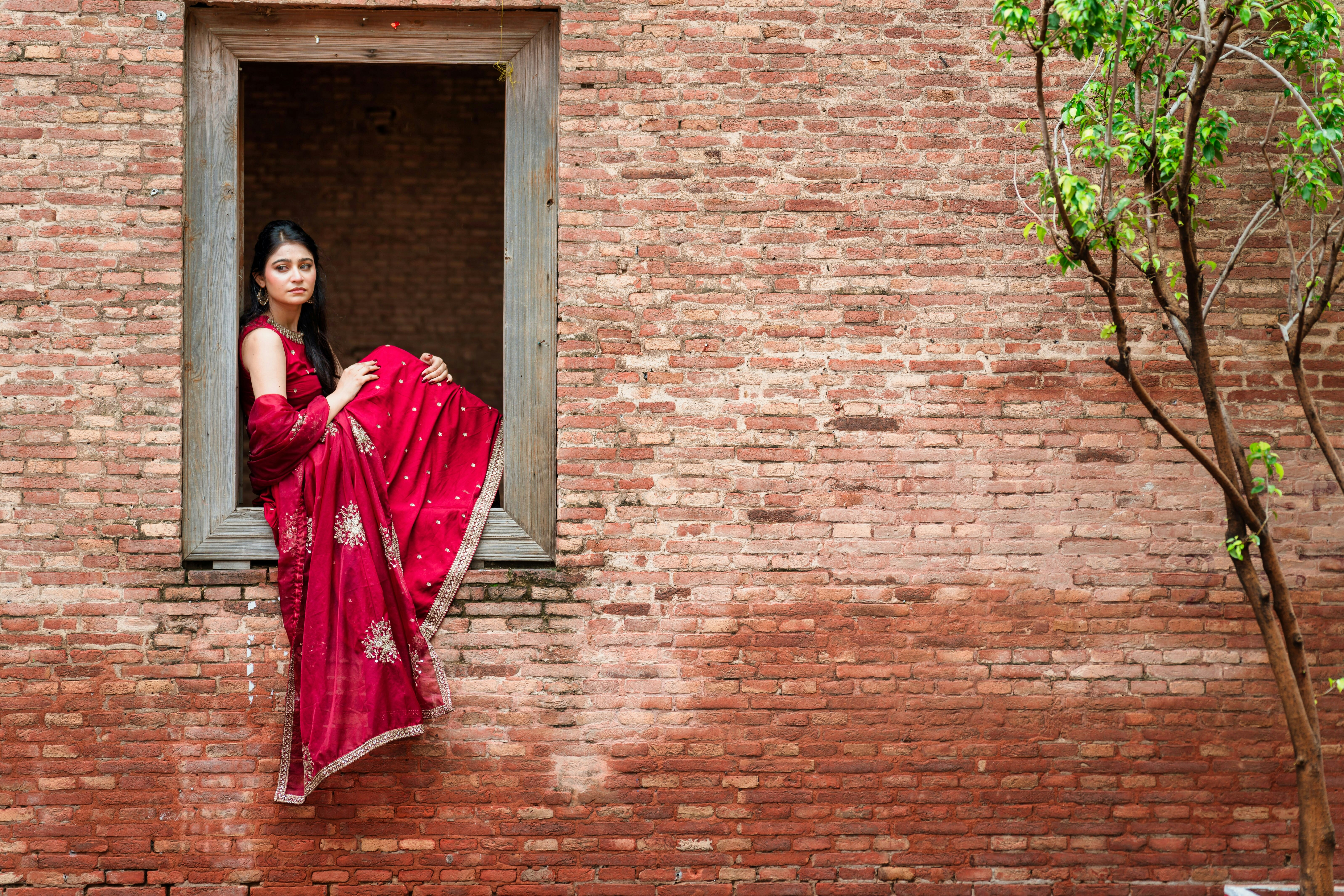A woman in a red embroidered sari sitting in a wooden window frame