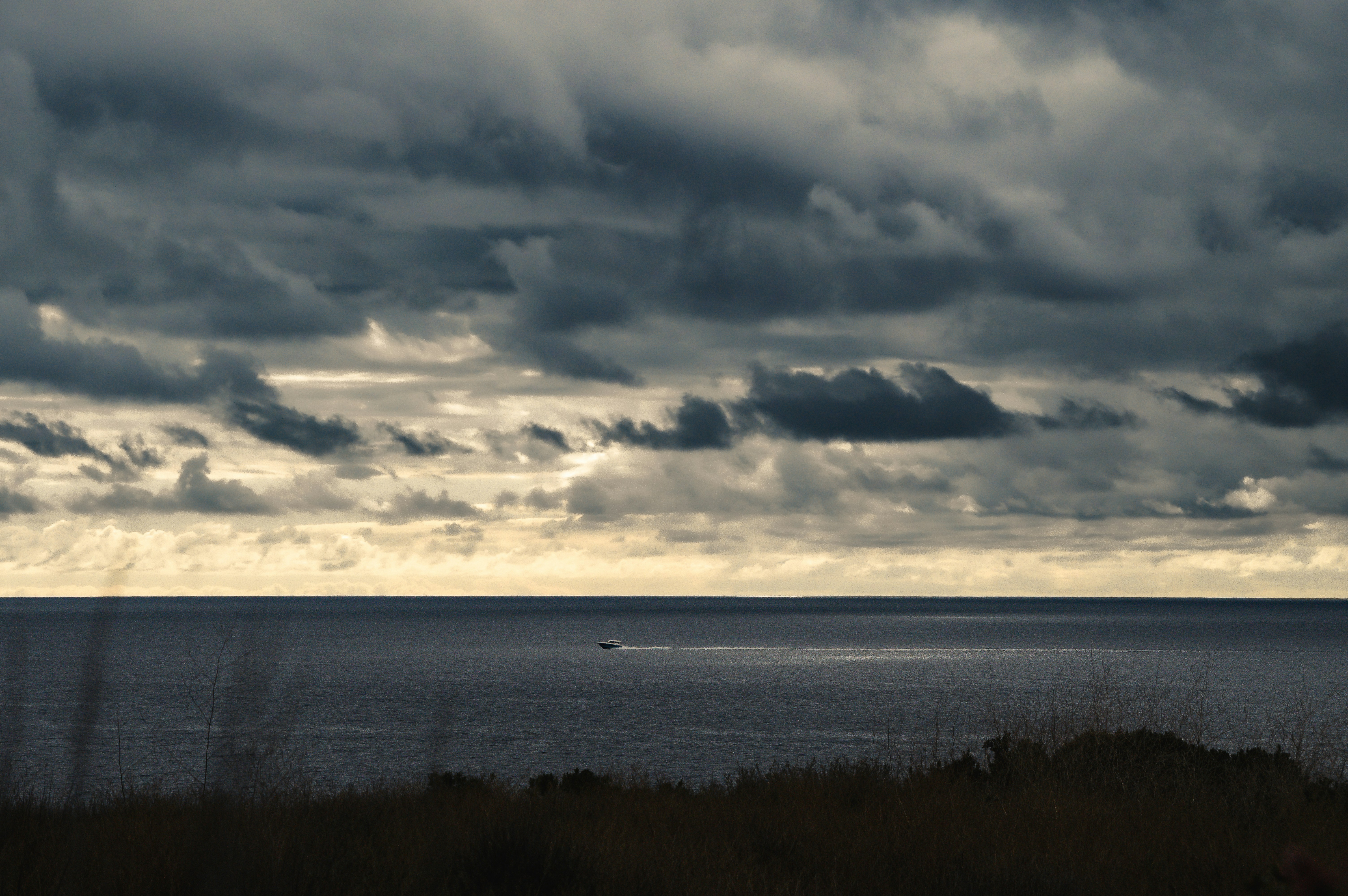 A small boat leaving a wake on the dark ocean under heavy storm clouds