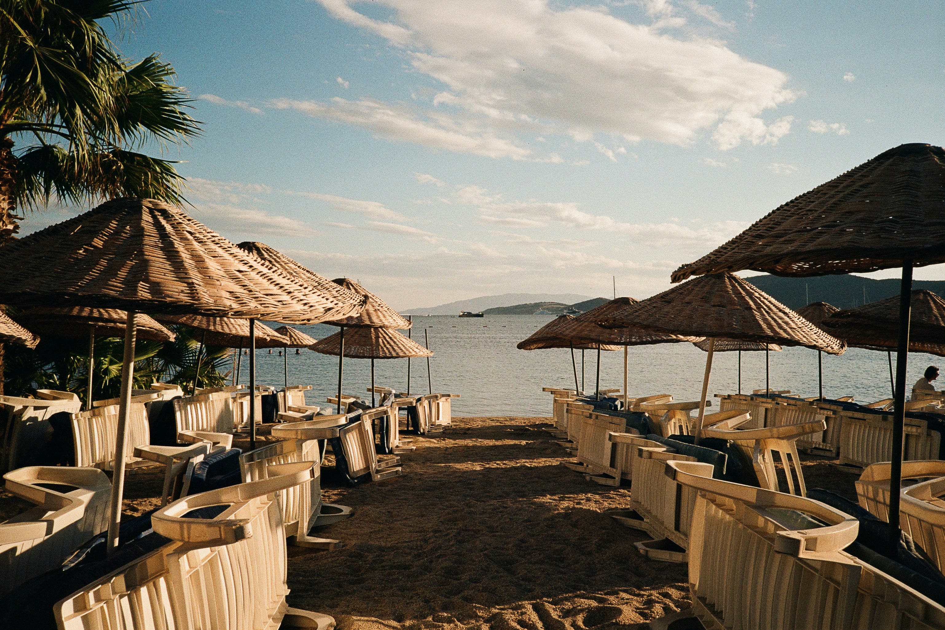 Straw umbrellas and white lounge chairs on a sandy beach in Bodrum, Türkiye