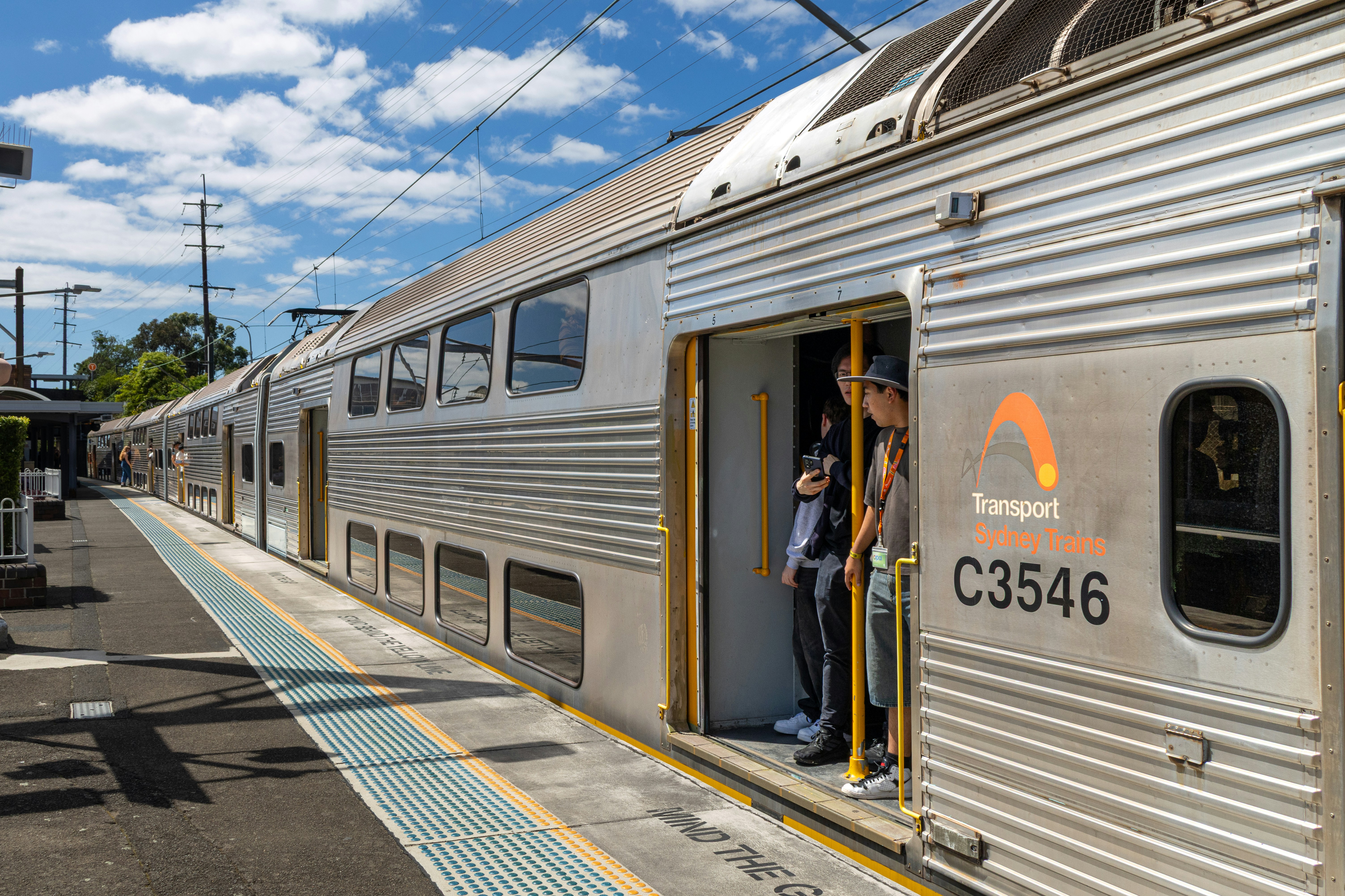 People standing in the open doorway of a silver Sydney Trains carriage at a platform