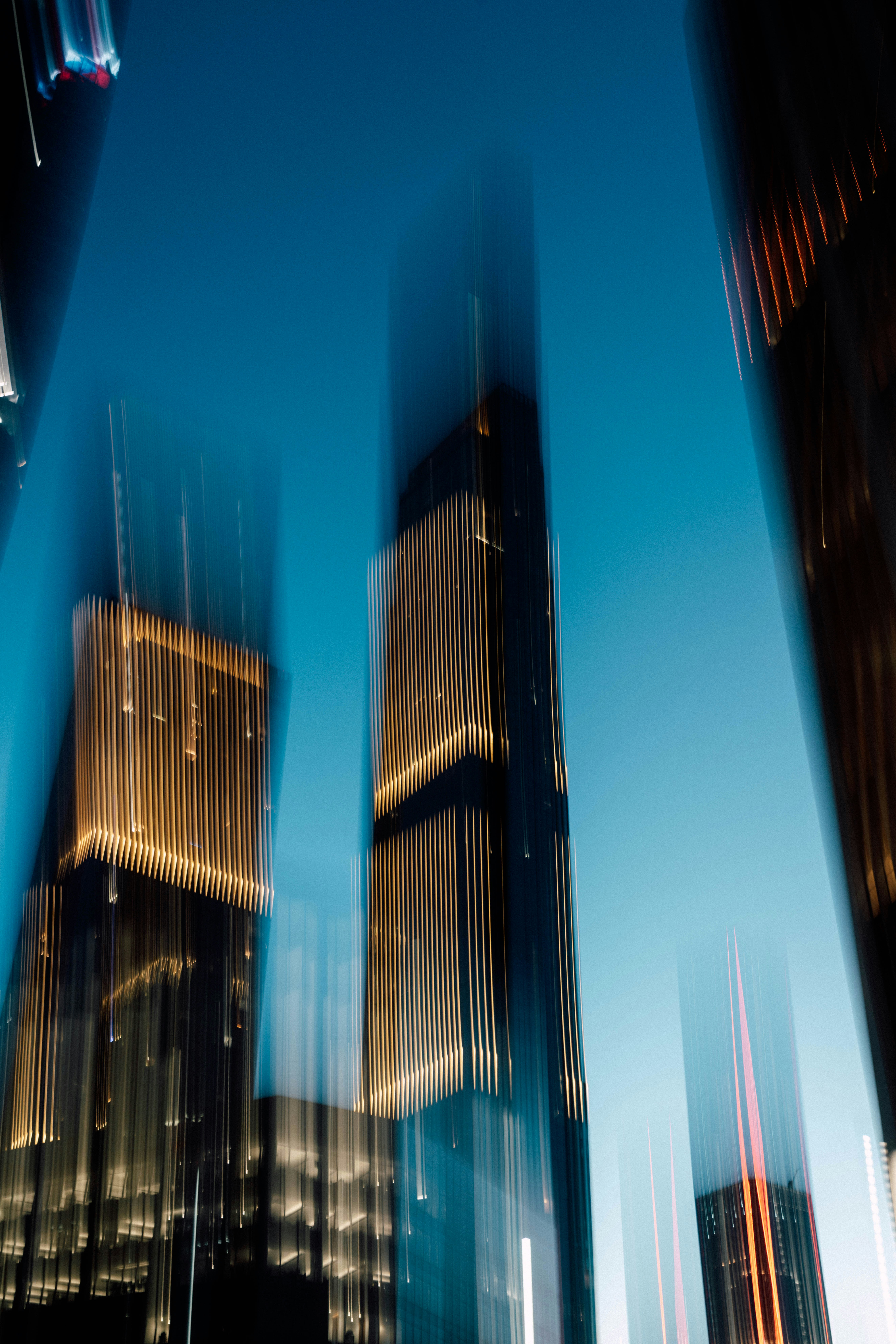 Tall skyscrapers with vertical golden lights against a deep blue sky in motion blur