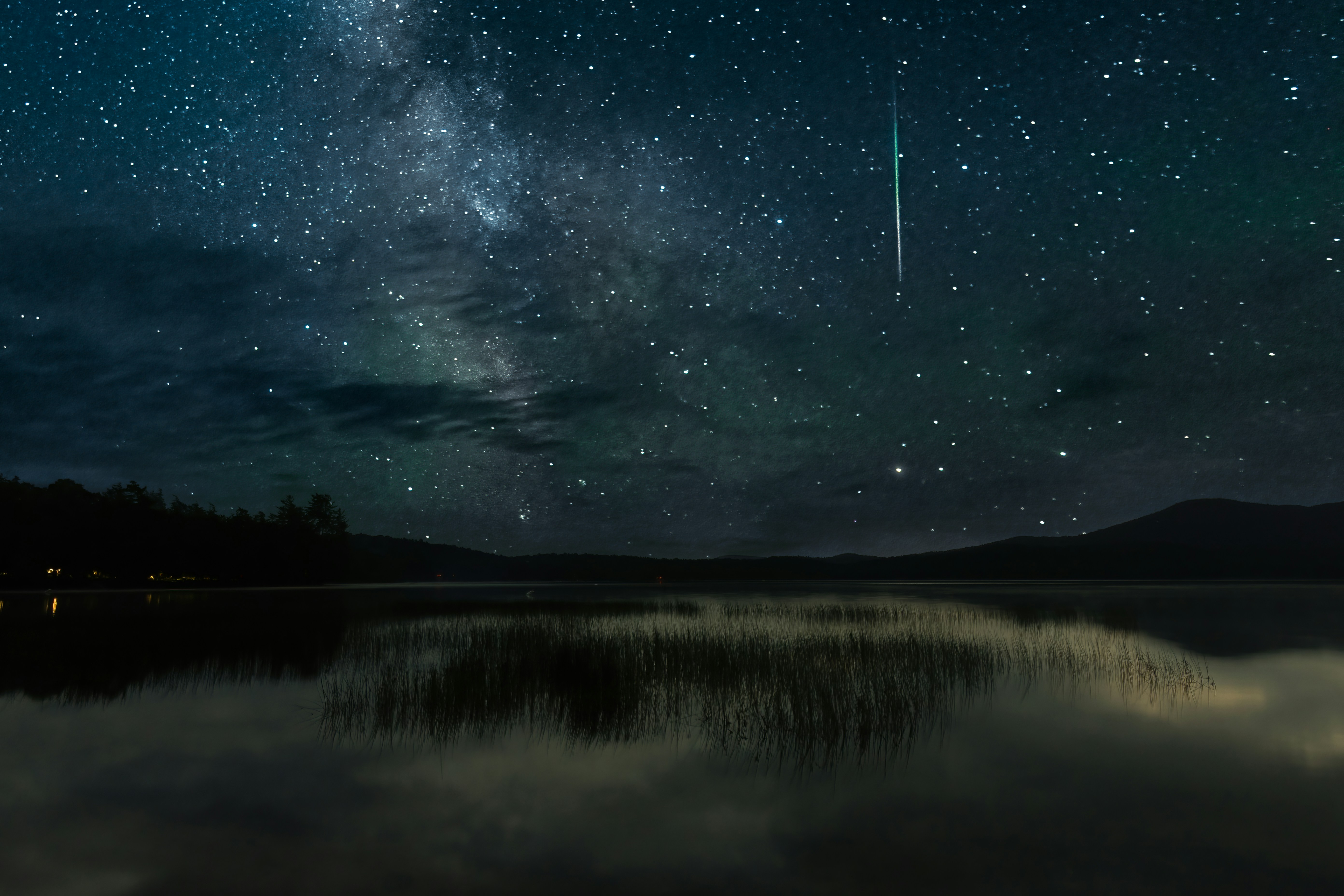 A bright meteor streaking across a starry night sky above a calm lake