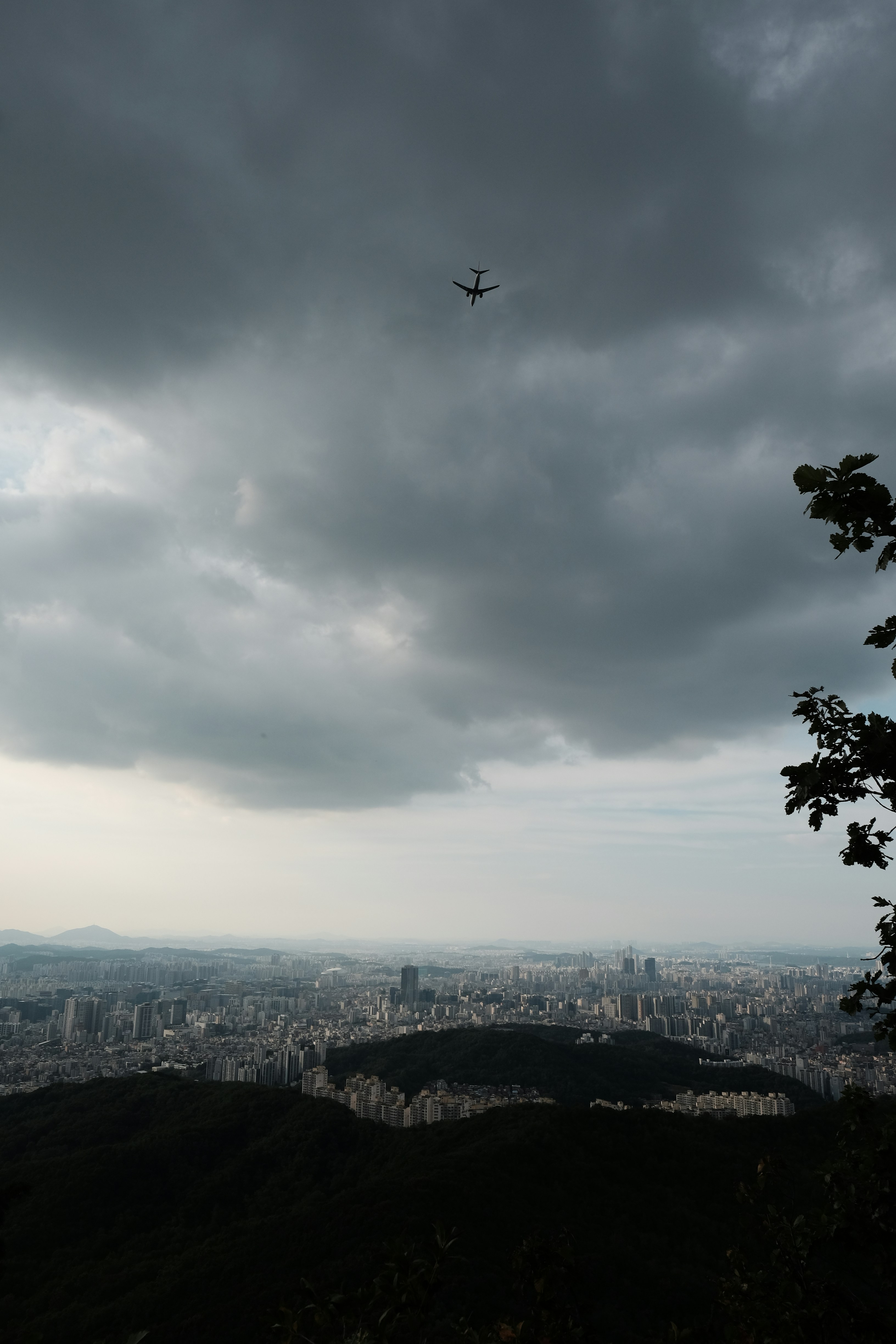 An airplane flying over a sprawling city under a dark, cloudy sky