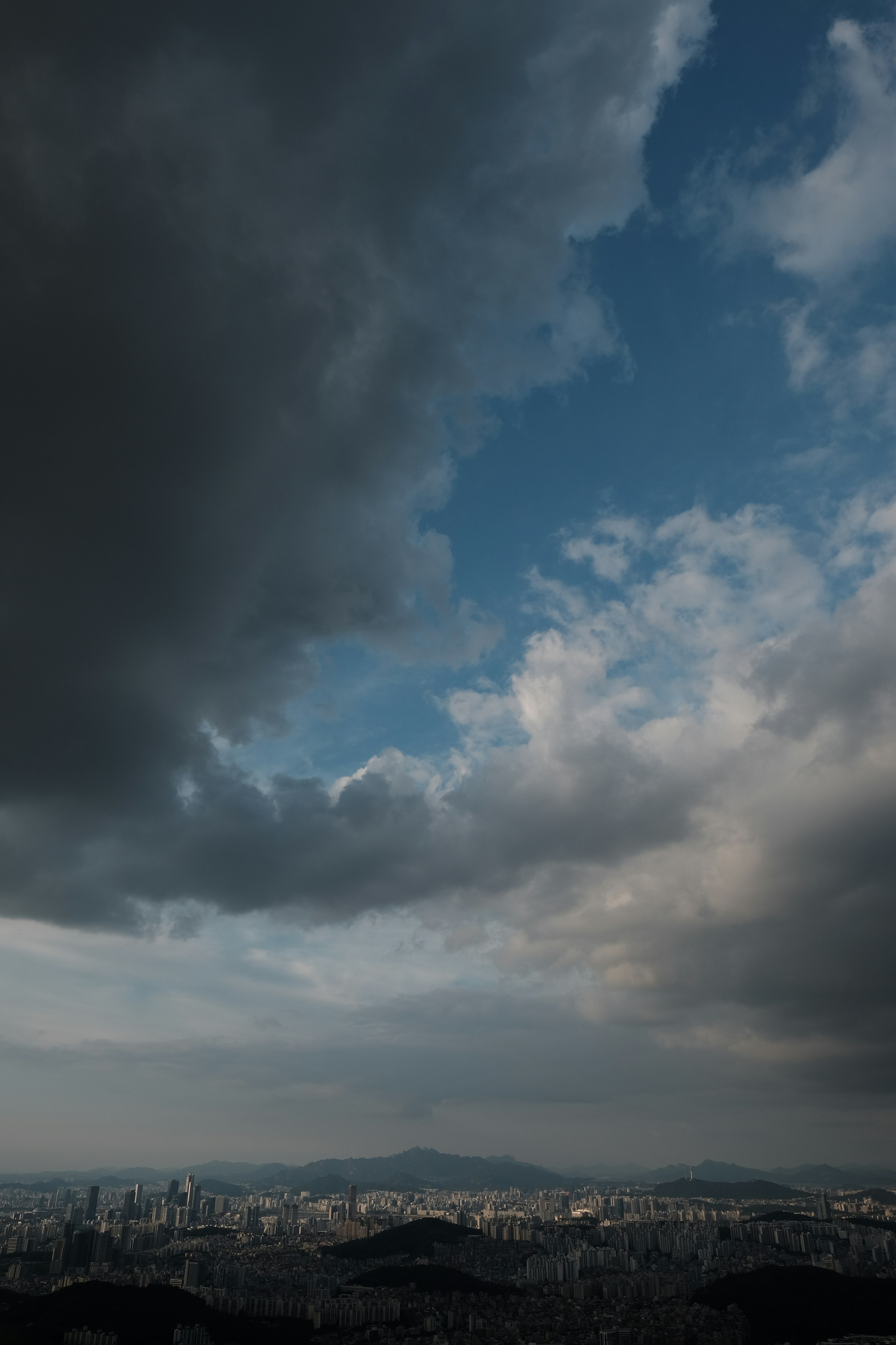 A sprawling city skyline under a vast sky with dark, heavy storm clouds