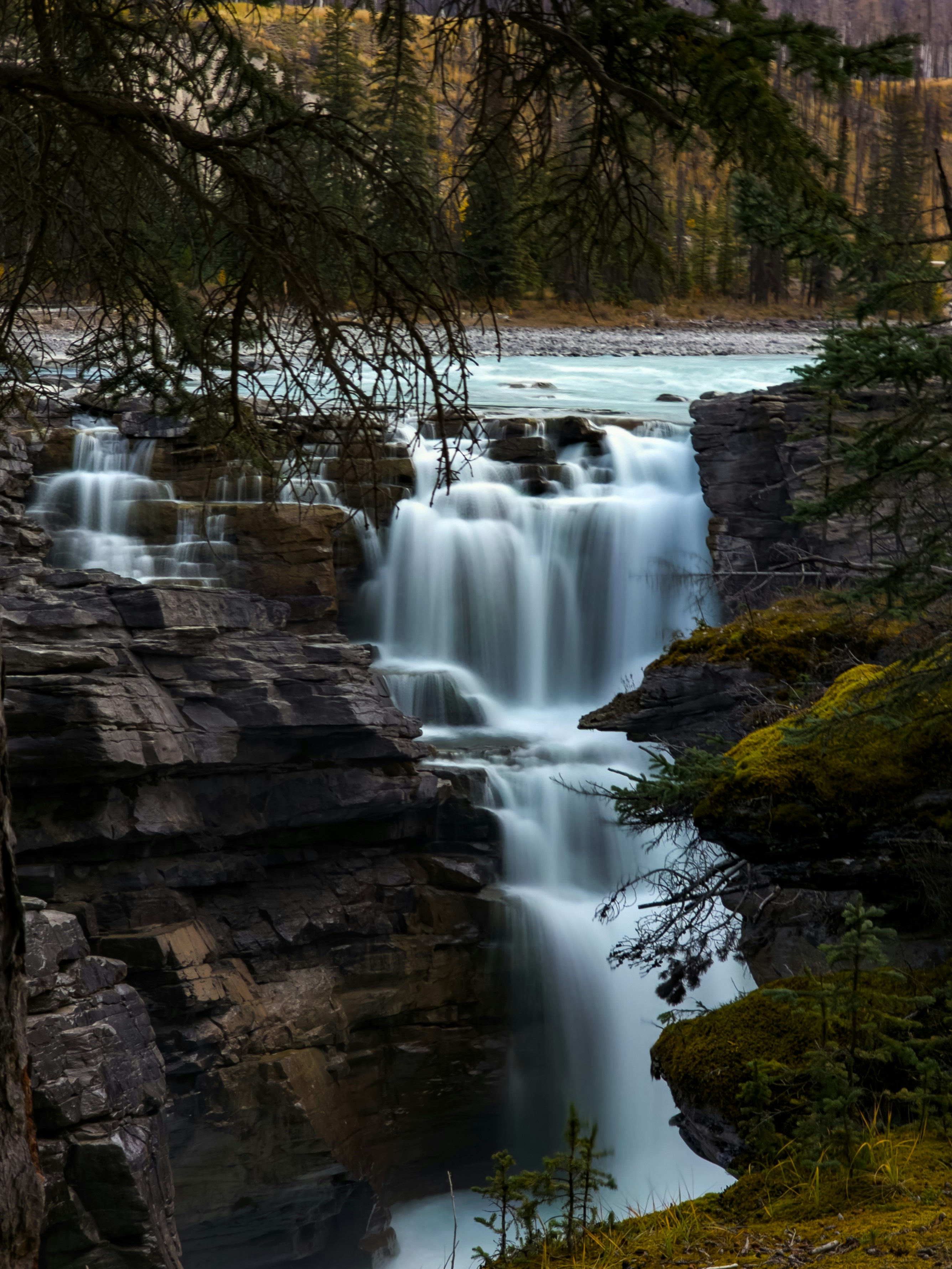 Long exposure of a tiered waterfall cascading over dark rocky cliffs into a river
