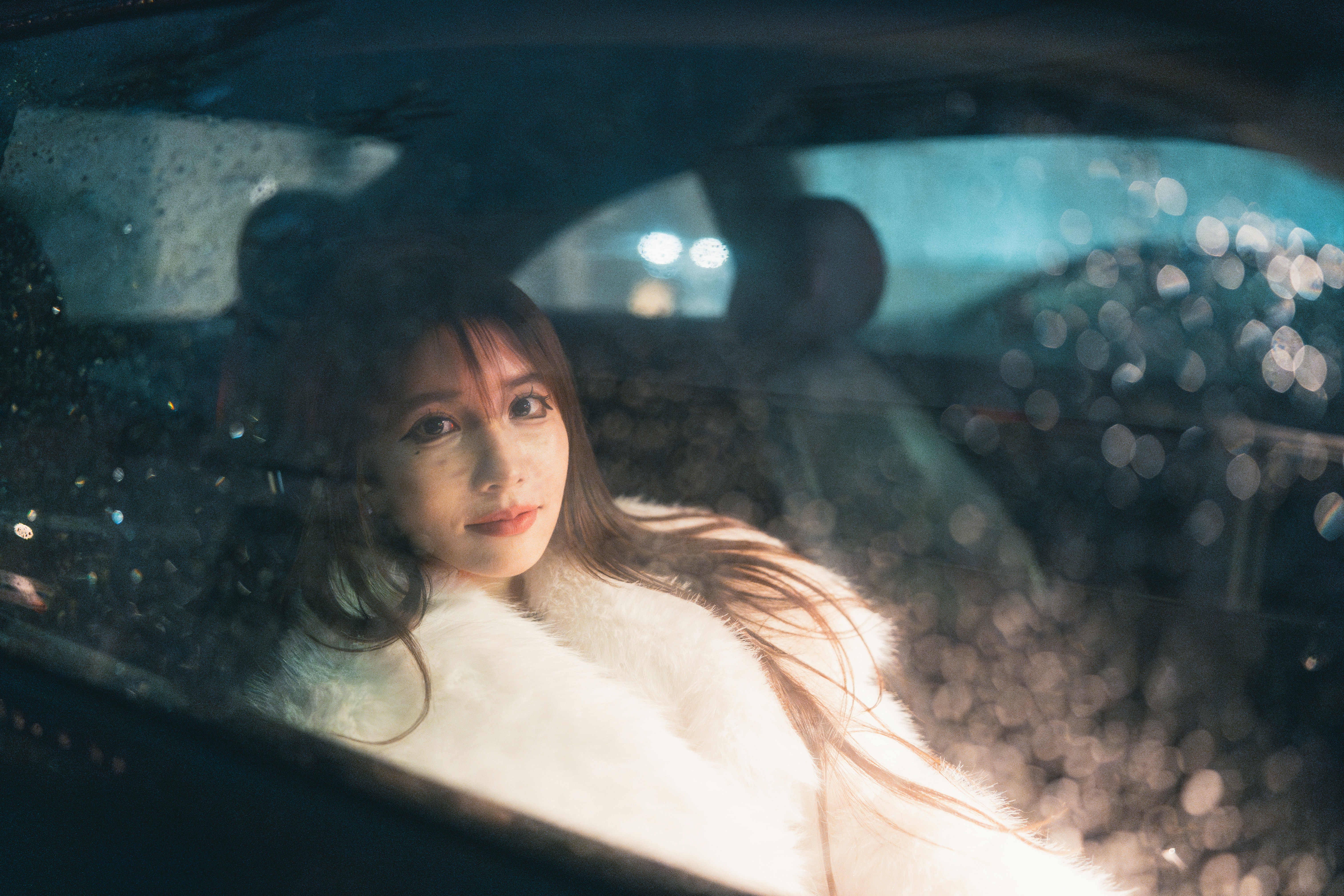 A woman in a white faux fur coat inside a car at night
