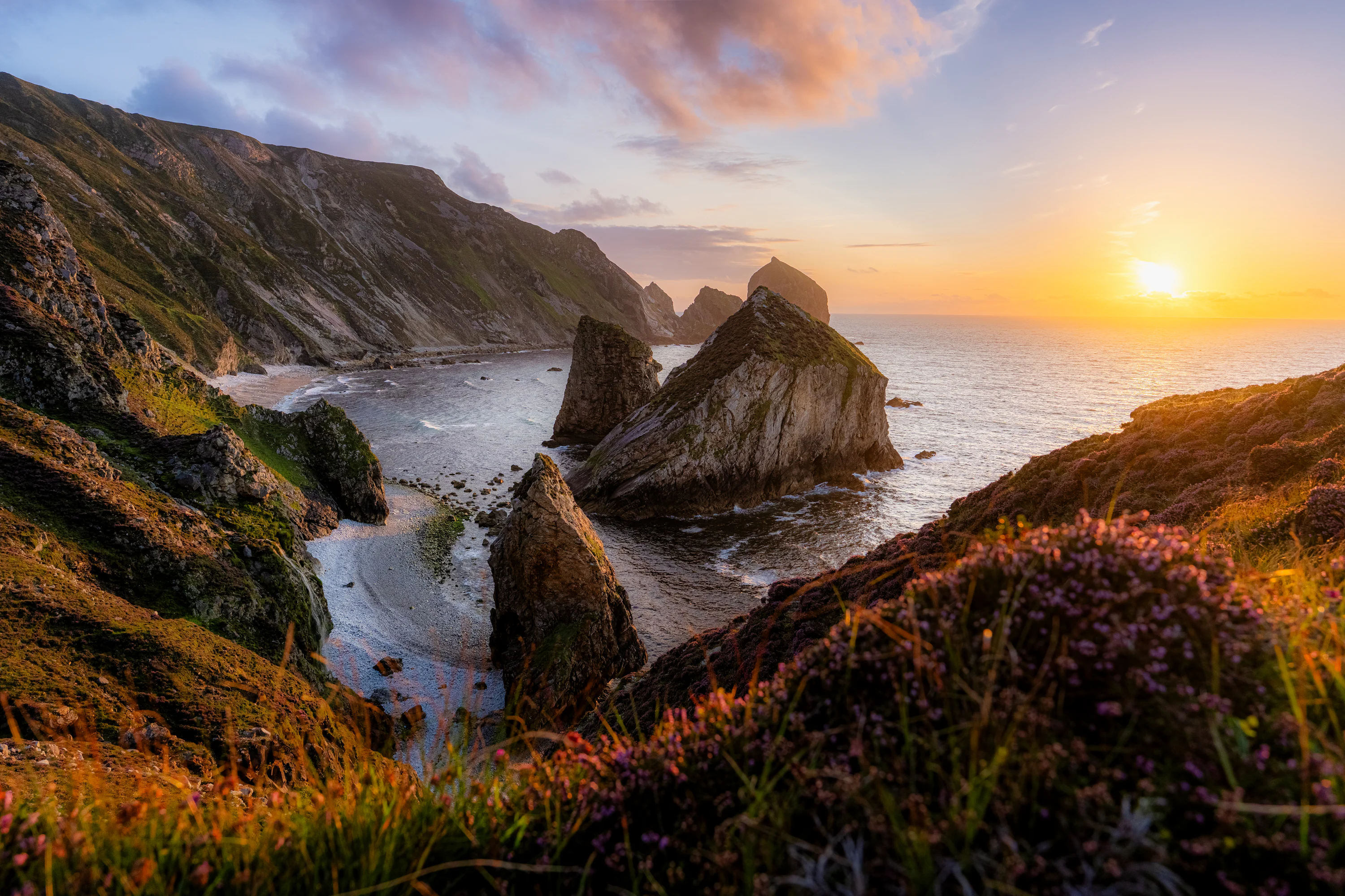 Rocky sea stacks in a cove under a warm orange sky at low sun