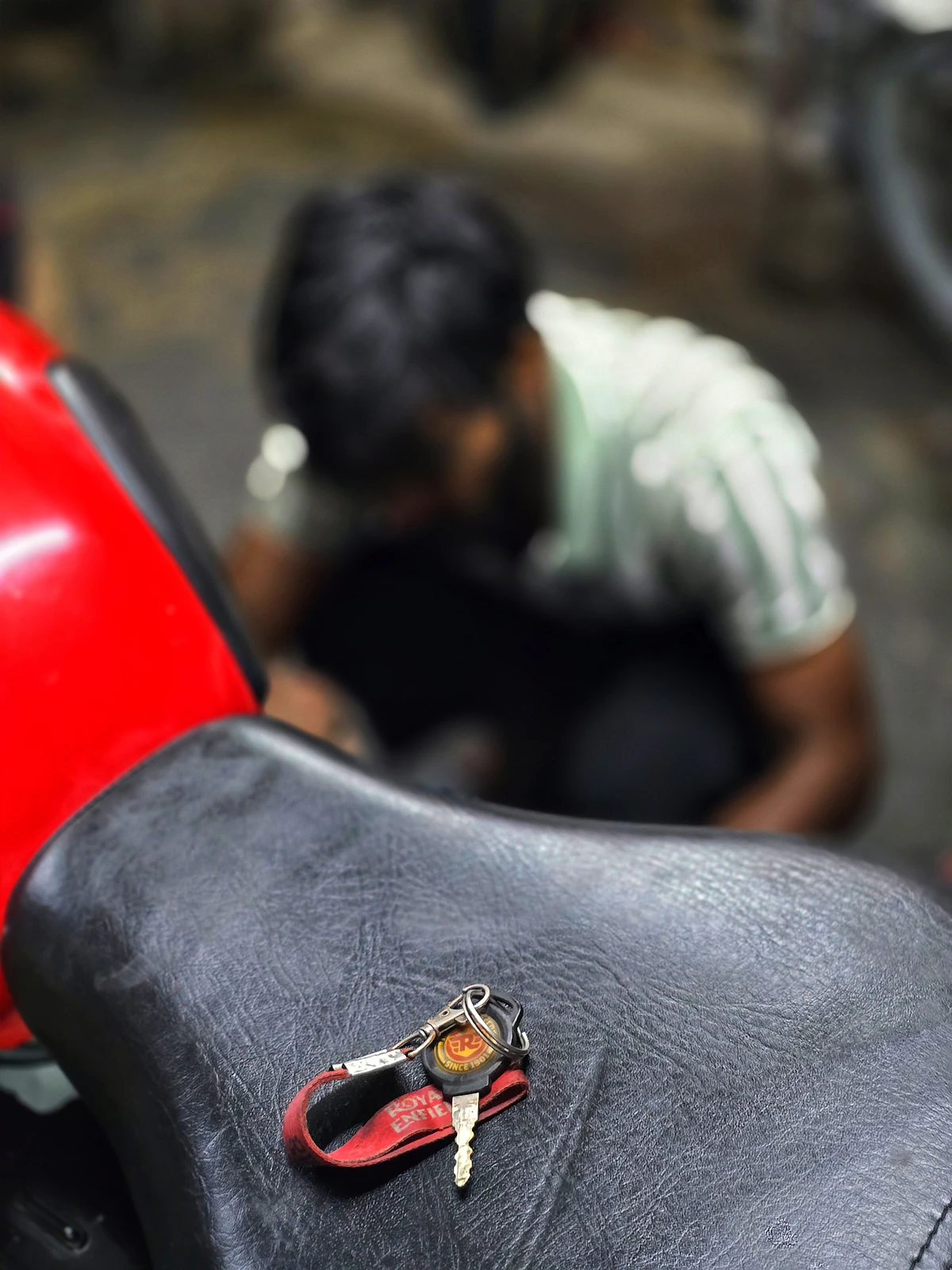 Kunci sepeda motor dengan gantungan kain merah di atas jok kulit hitam.
