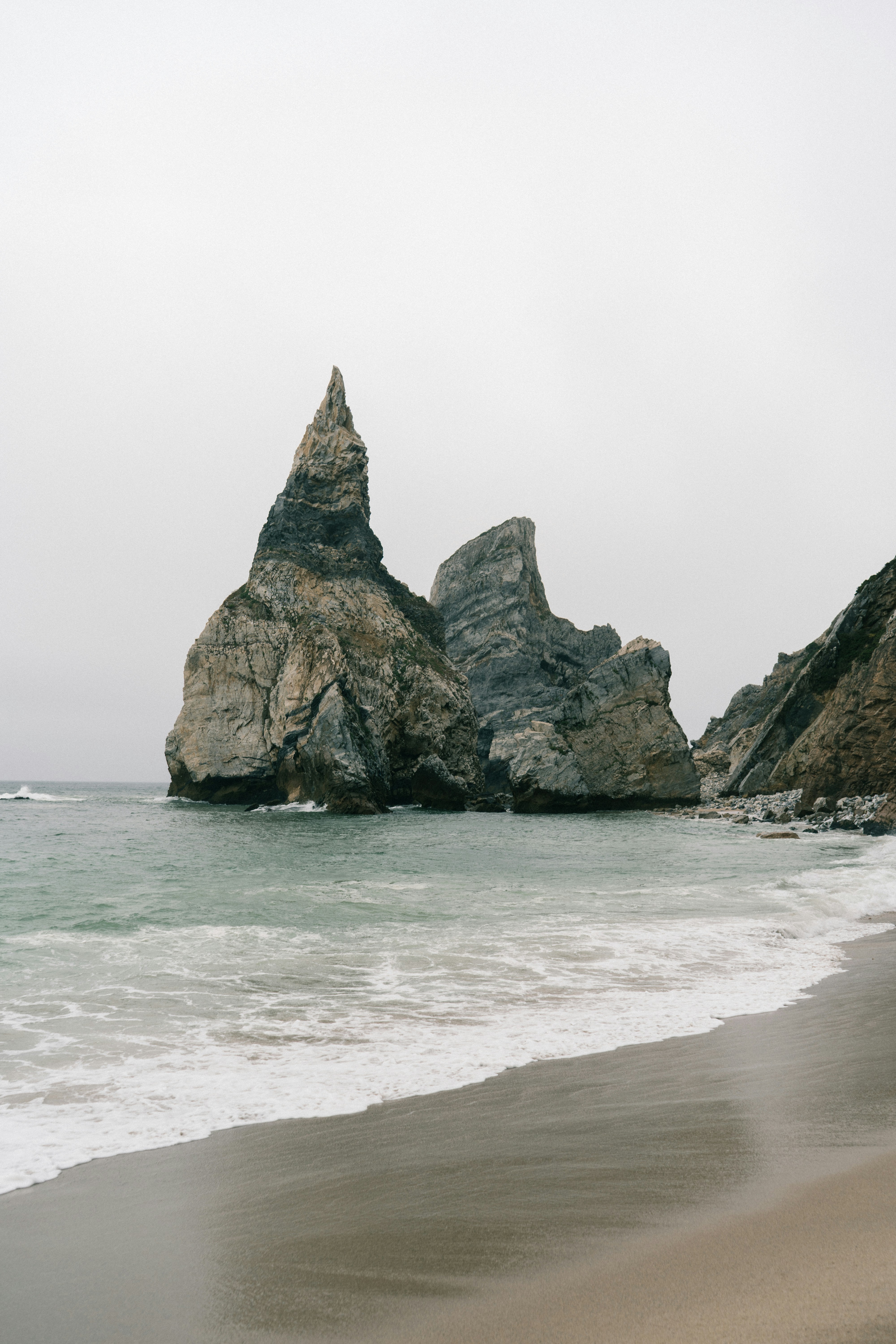 Jagged rock formations rising from the ocean on a sandy beach under overcast skies