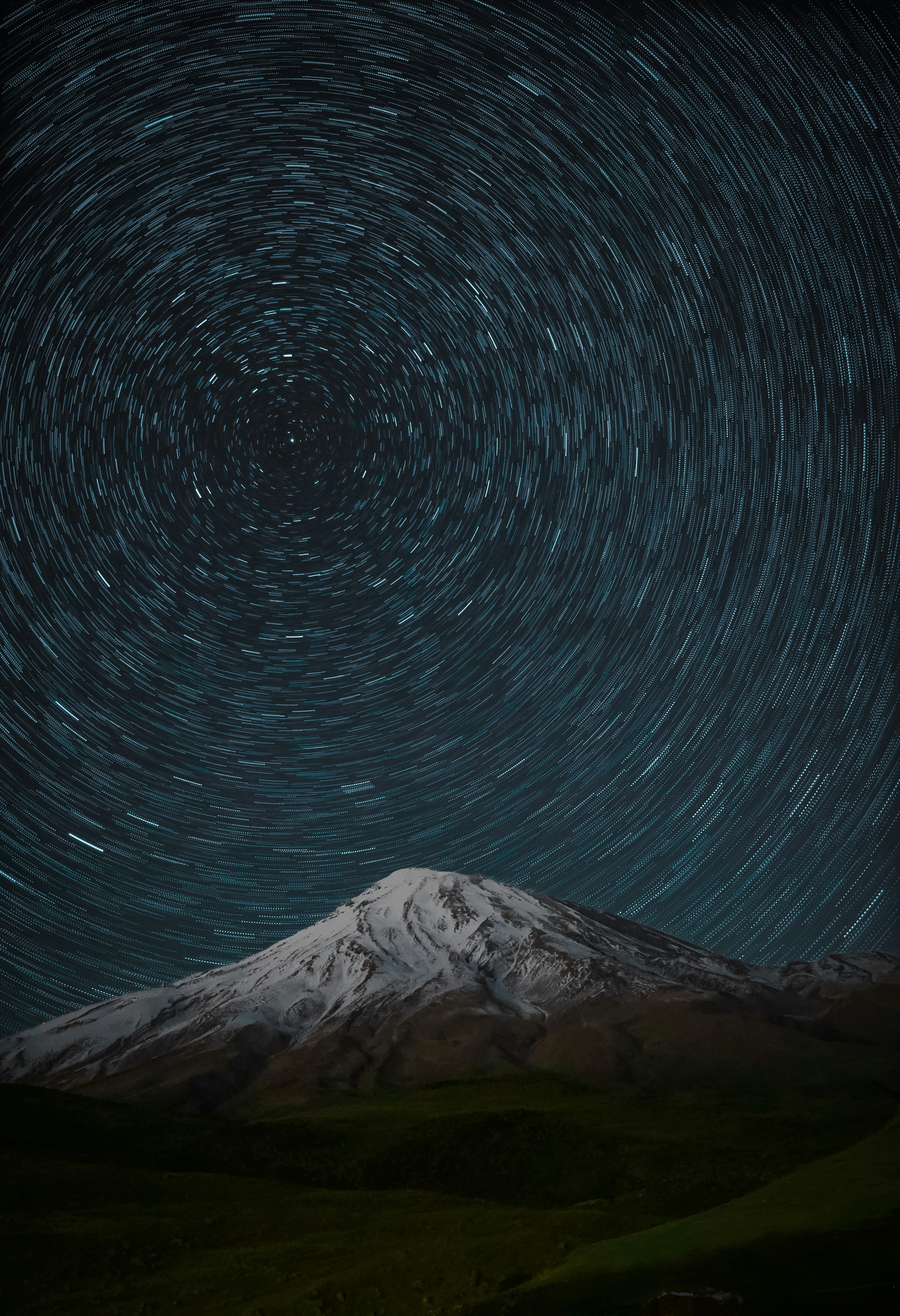 Circular star trails in the night sky above a snow-capped mountain peak