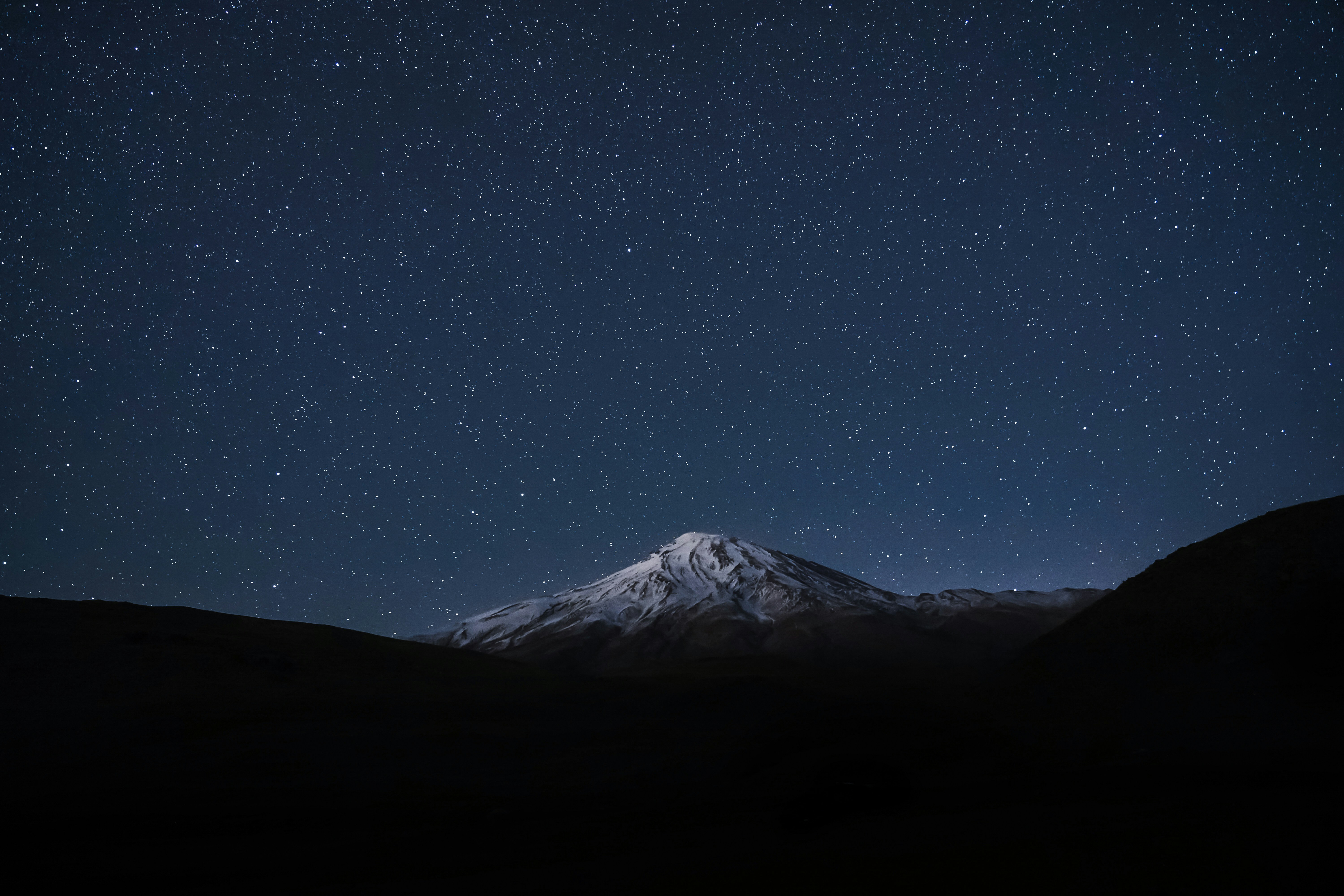 A snow-capped mountain peak under a vast night sky filled with bright stars