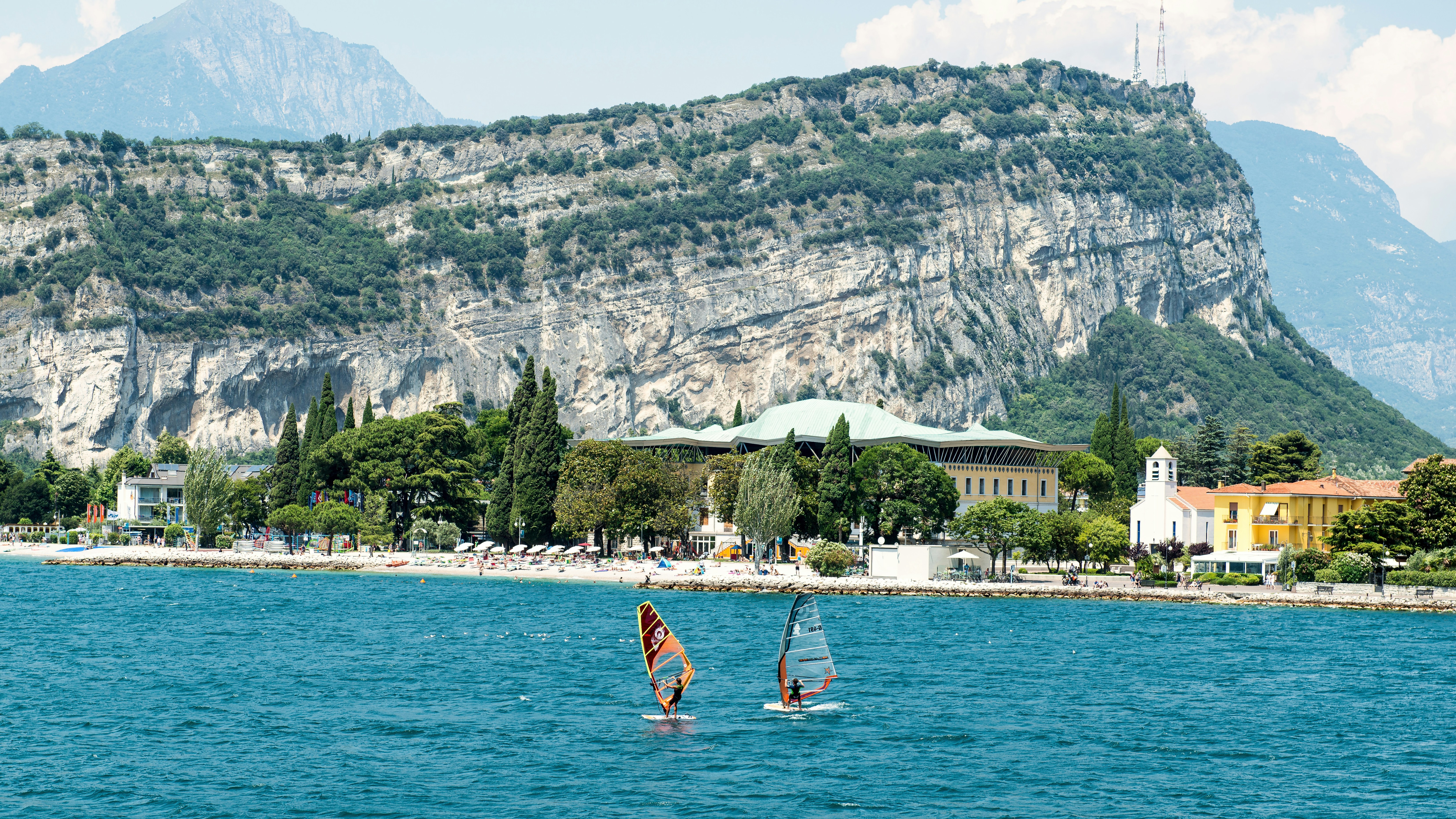 Two windsurfers on Lake Garda with a large rocky mountain in the background