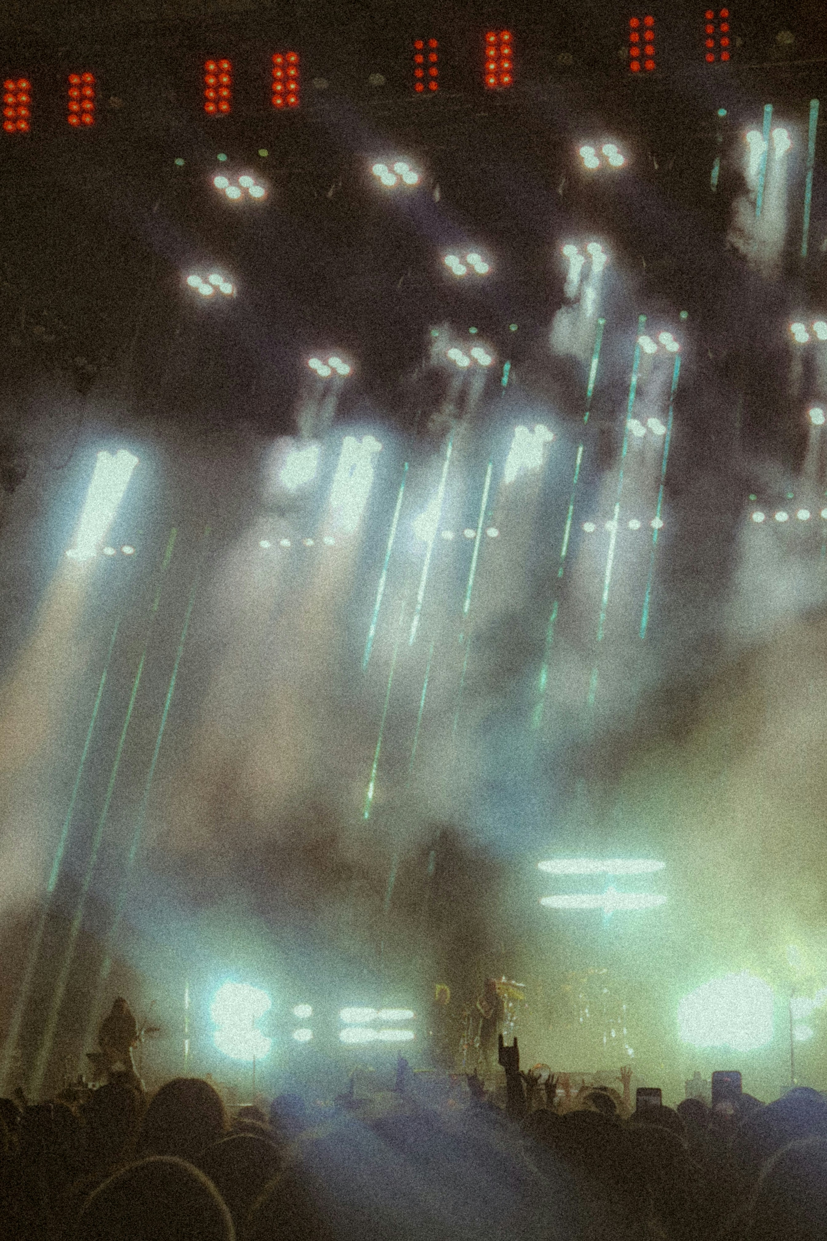 A crowd at a concert under bright stage lights and thick atmospheric smoke