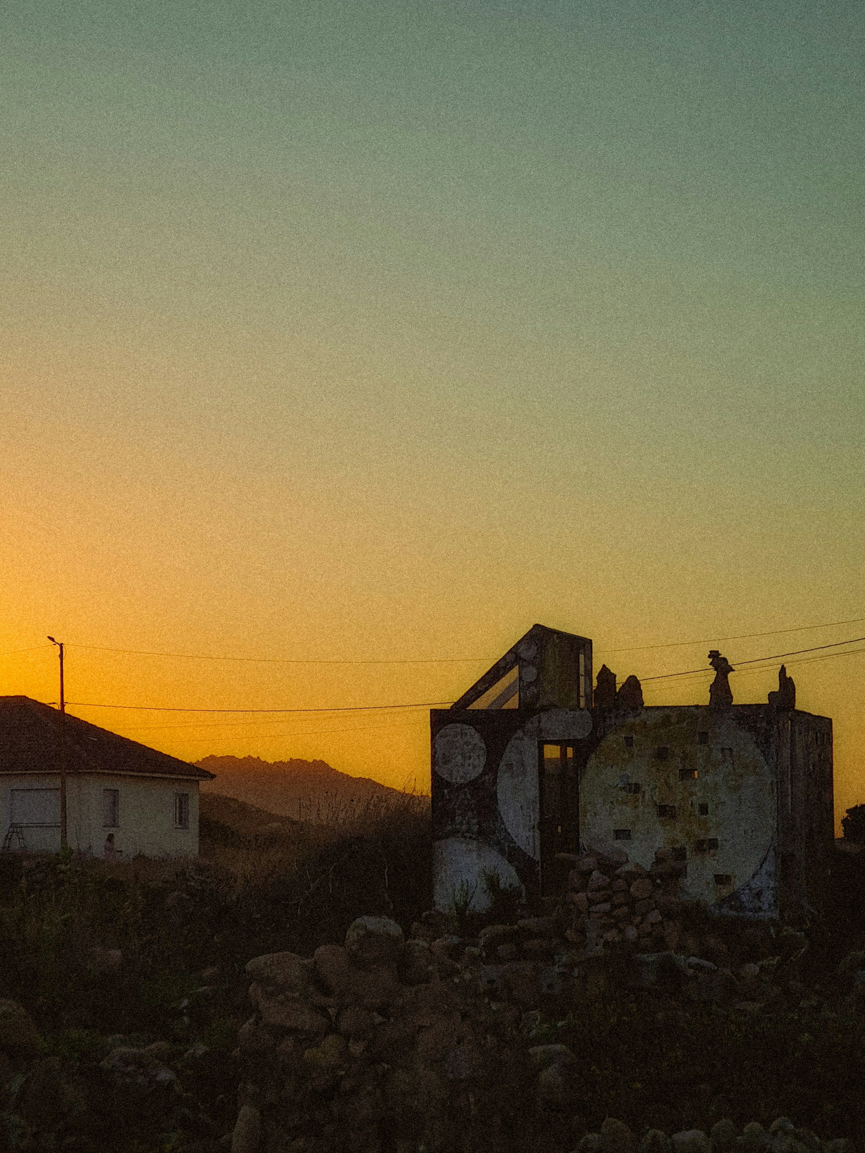 A weathered structure with circular patterns against a warm orange sky at low sun