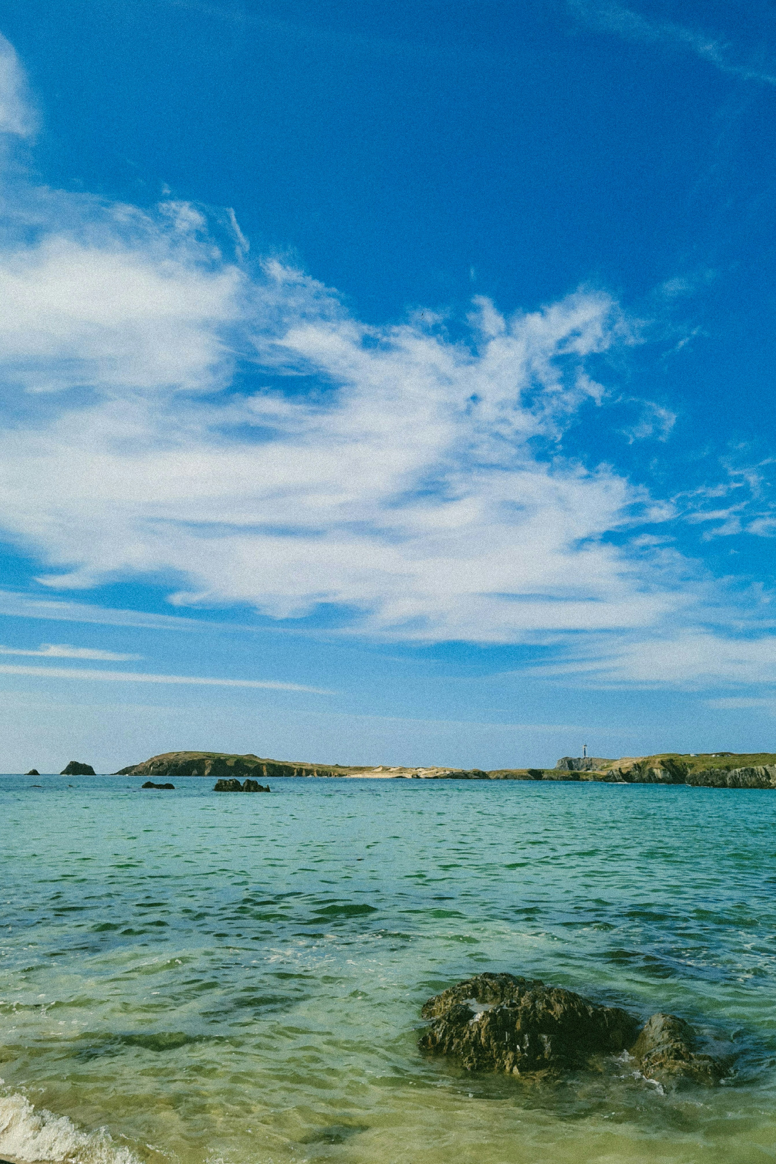 Clear turquoise water with rocky outcrops under a bright blue sky with clouds