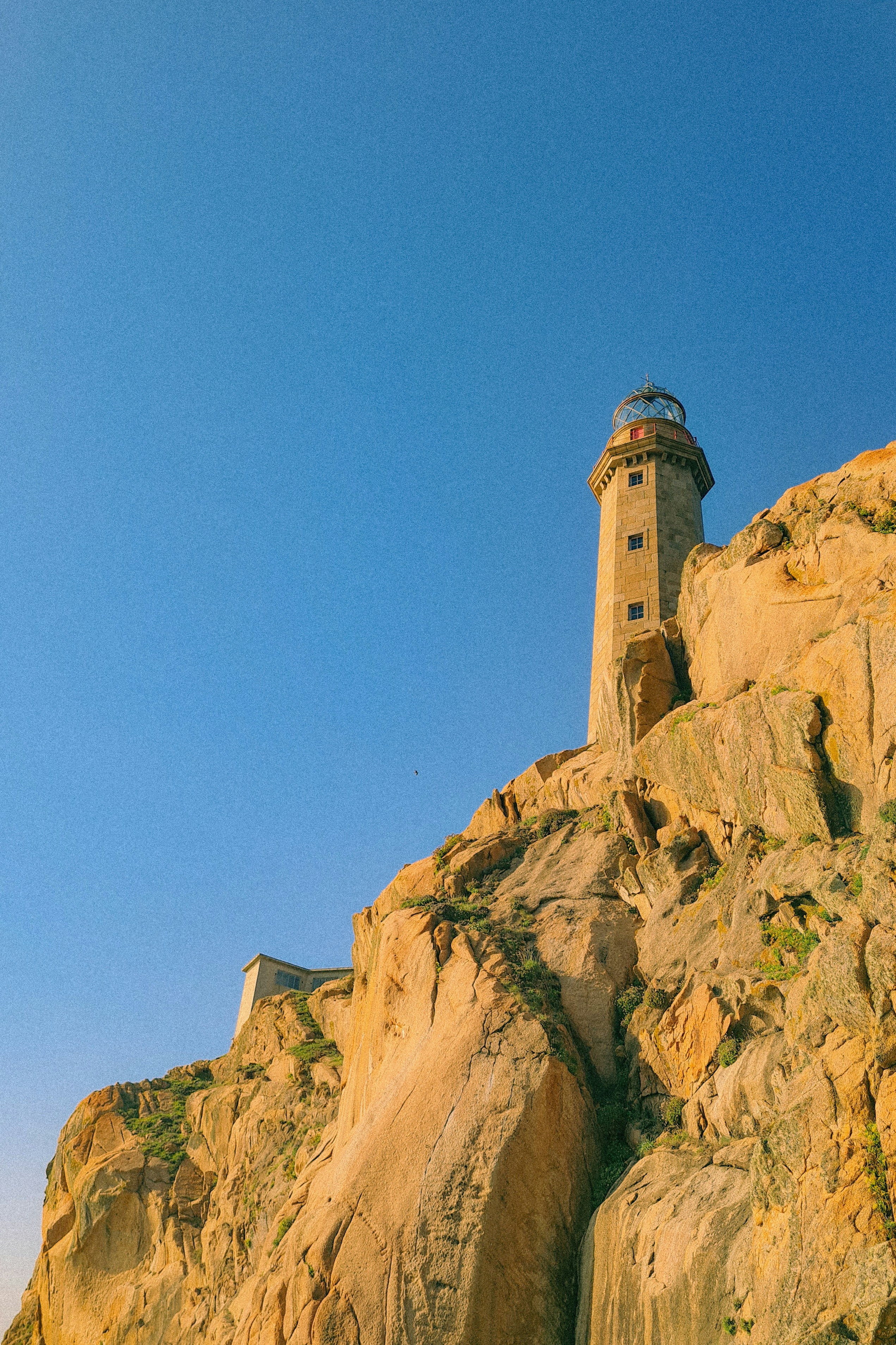 A stone lighthouse on a rocky cliff against a clear blue sky