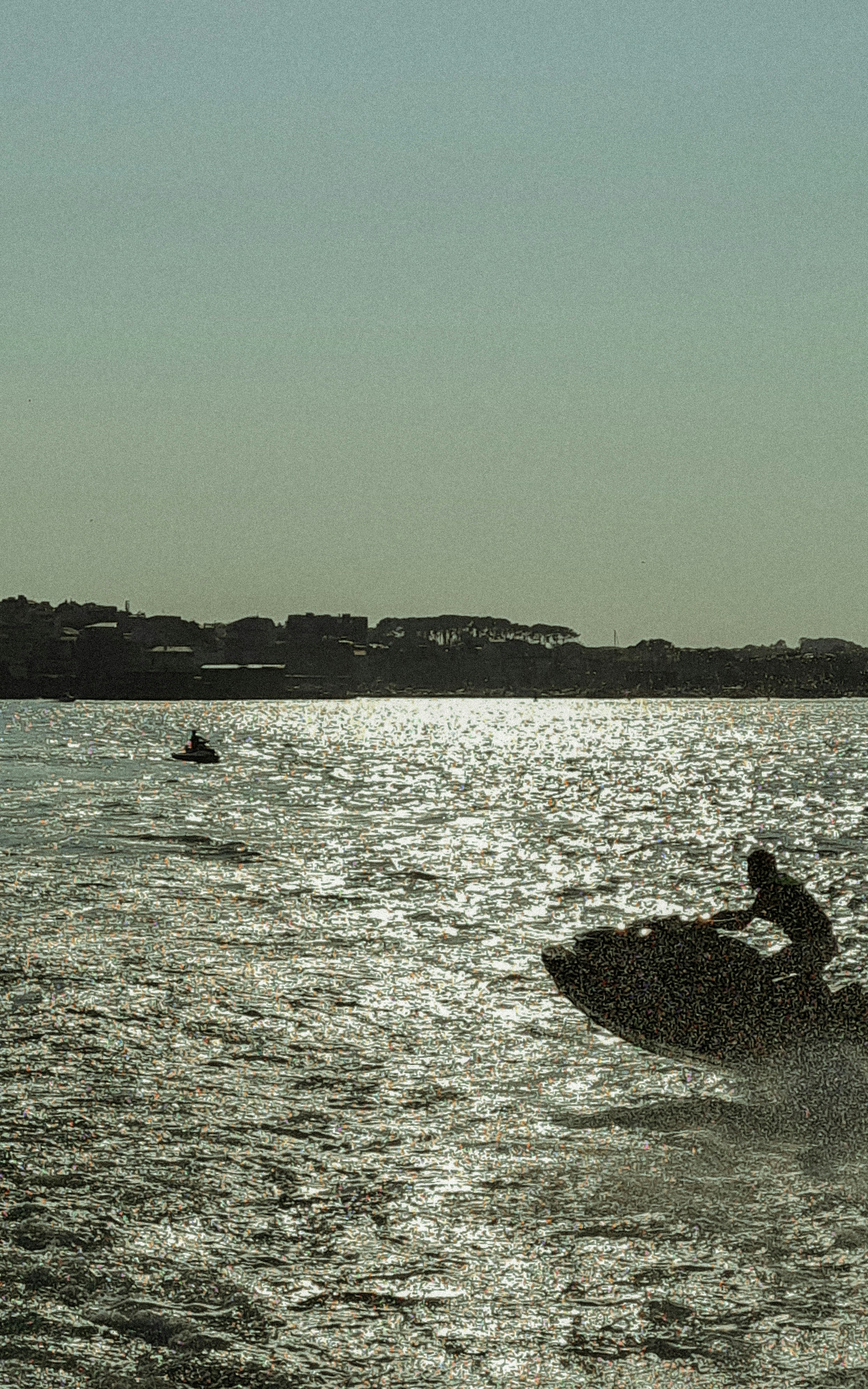 Two people riding jet skis on sparkling water under a bright sky