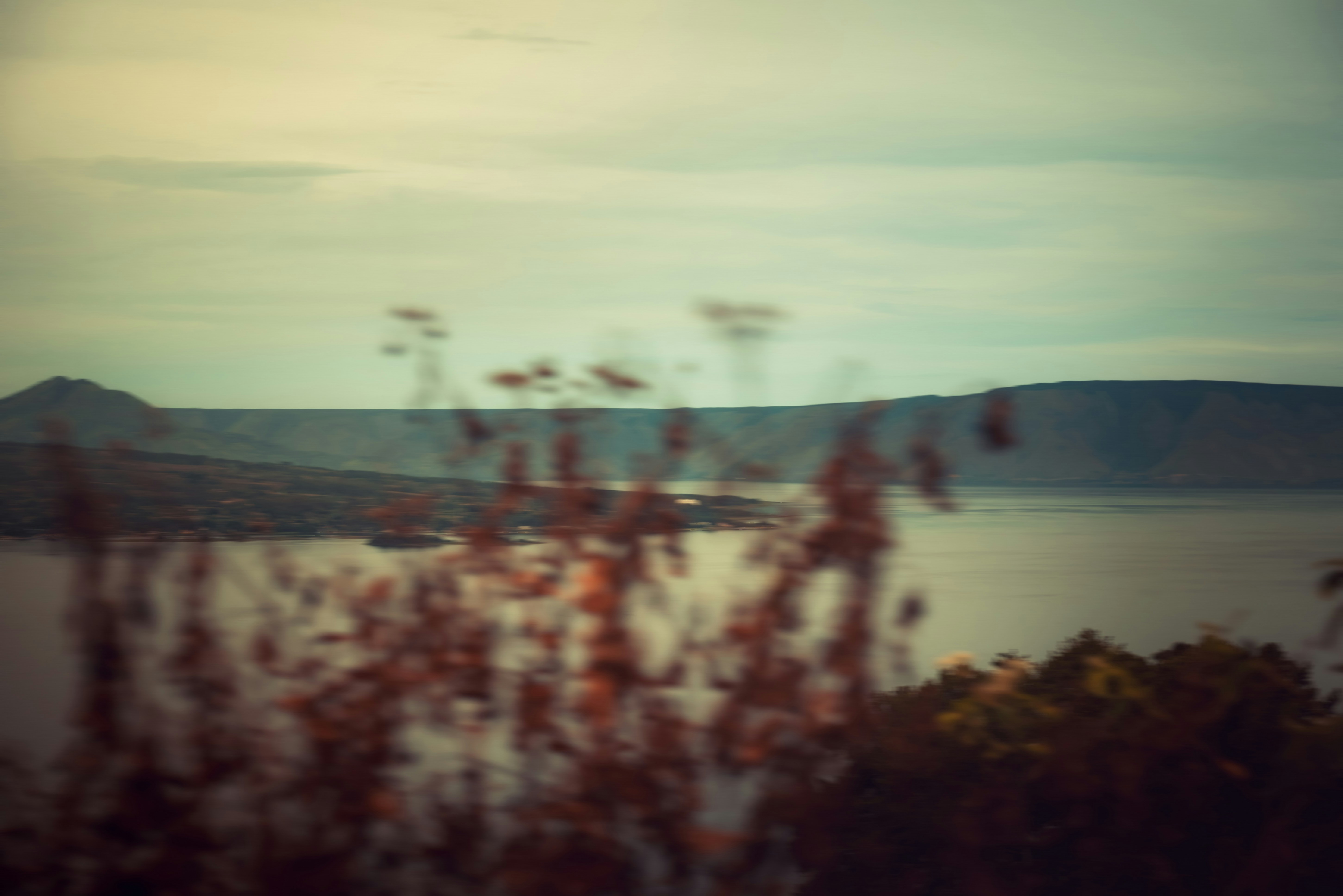 A calm lake surrounded by distant hills under a soft overcast sky