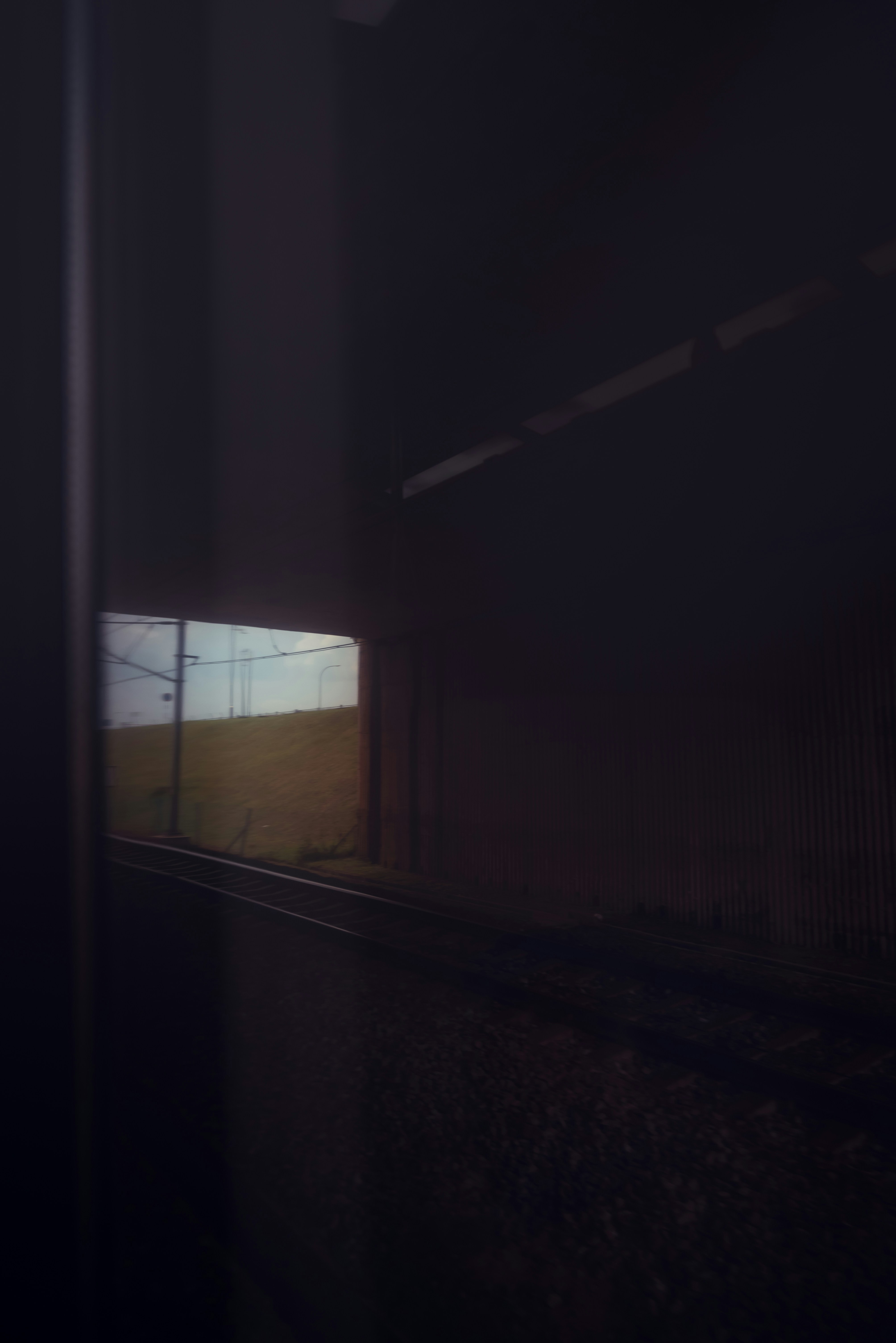 Railway tracks emerging from a dark tunnel into a grassy landscape